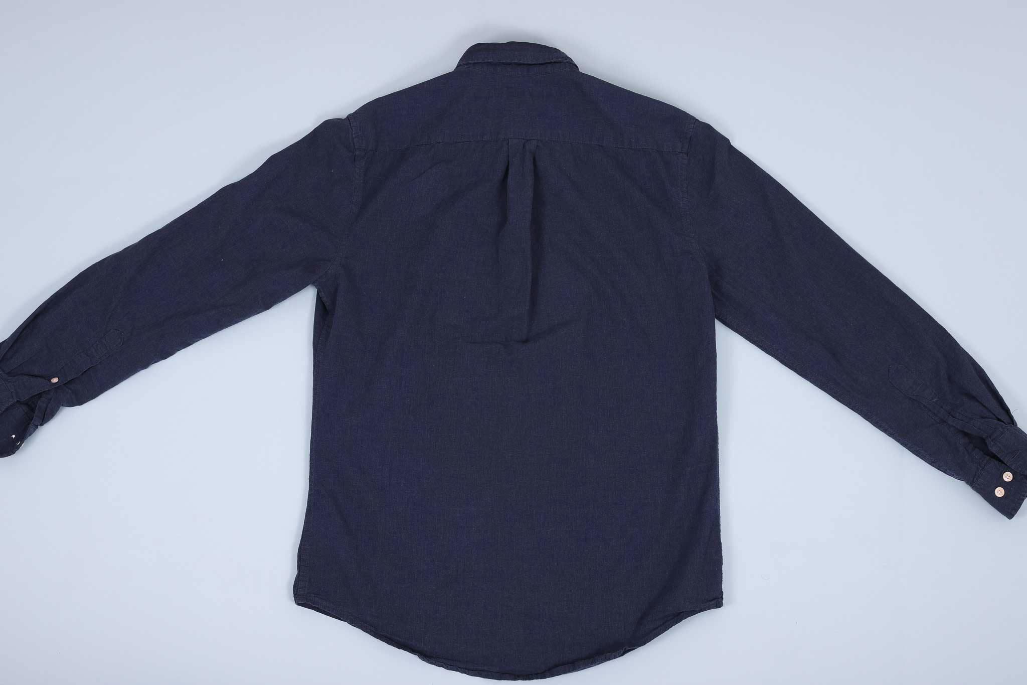 Navy buttoned up shirt spread out facing down against a light blue background Navy buttoned up shirt spread out facing down against a light blue background