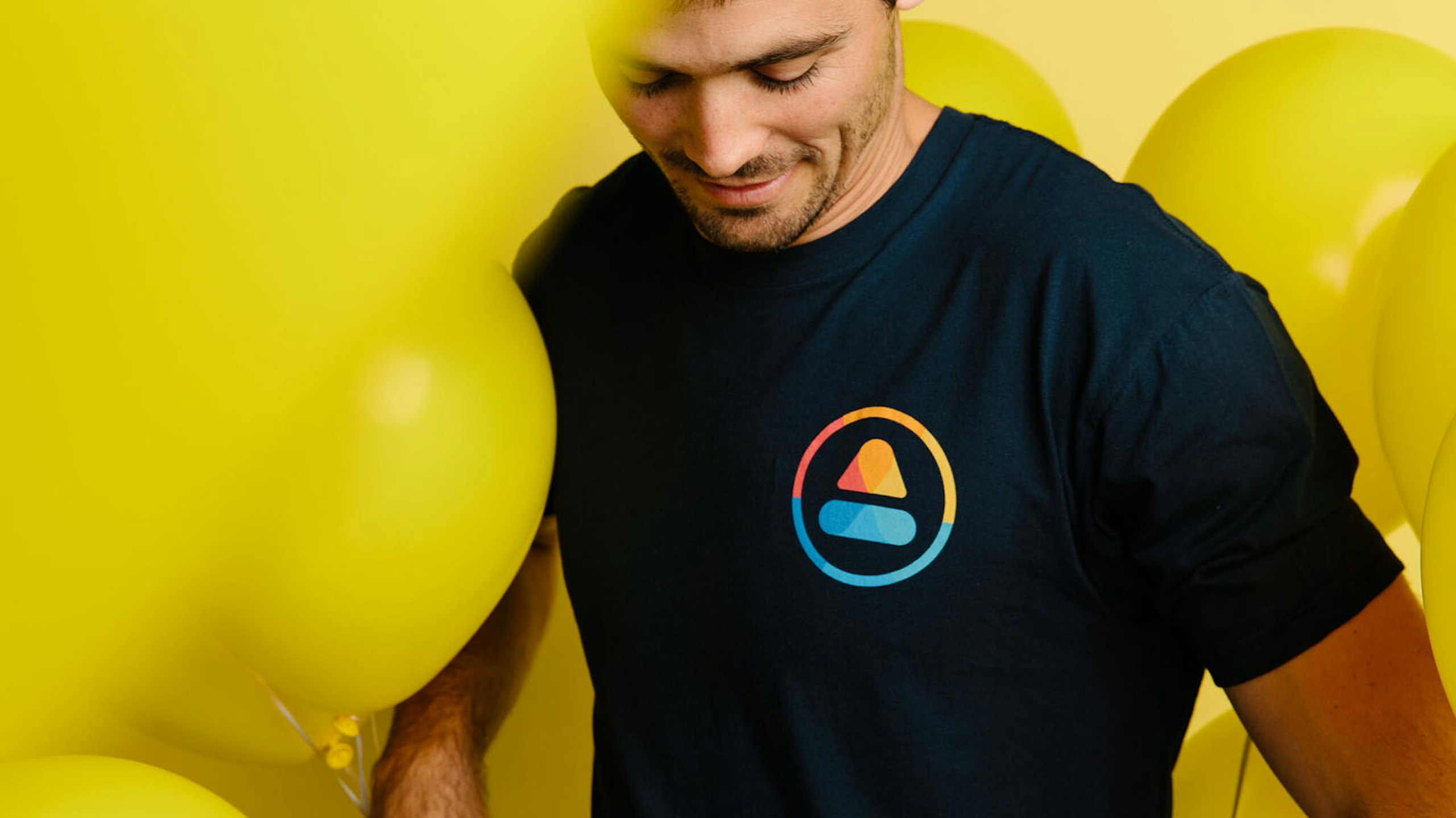 man wearing a black t-shirt in front of yellow balloons 