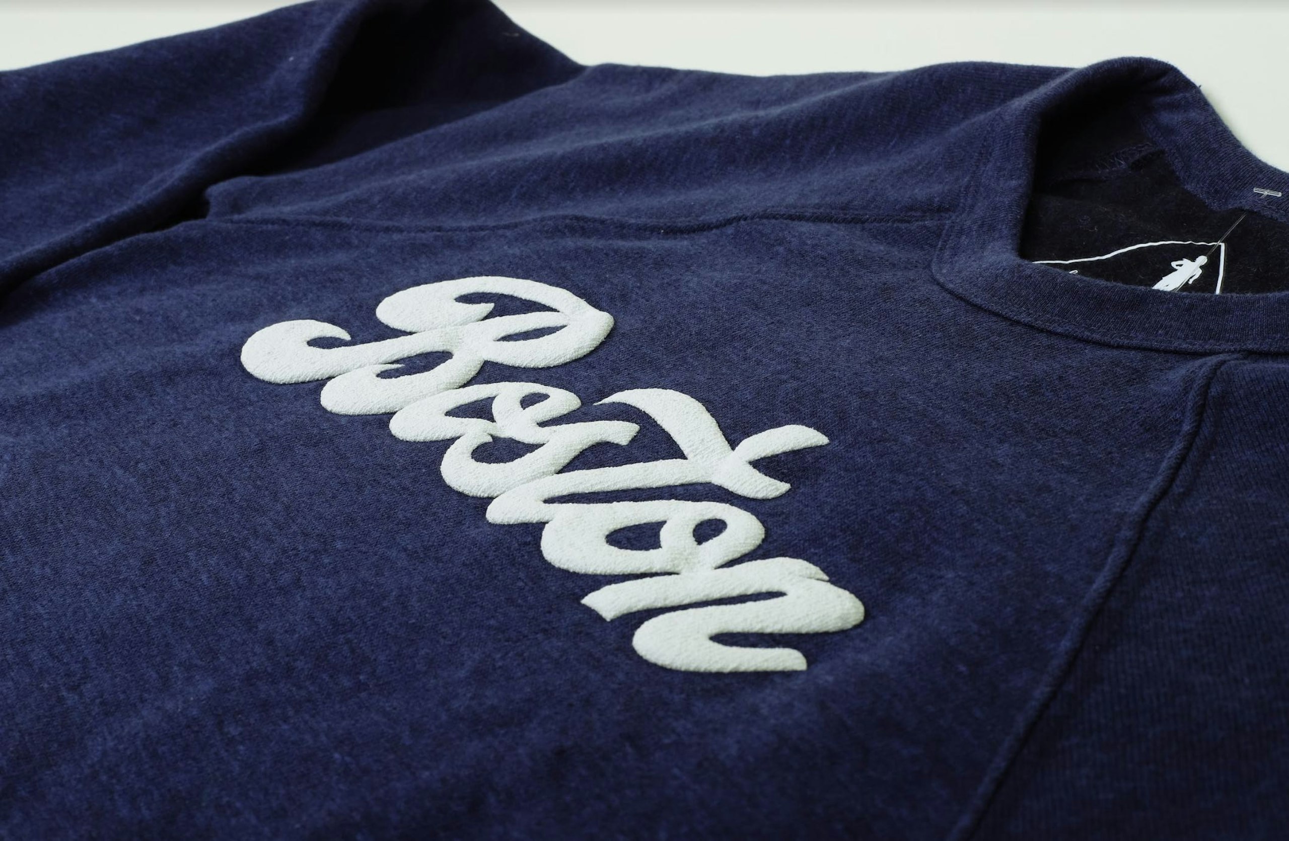 a white word "boston" printed in puff print on a navy t-shirt in a script font