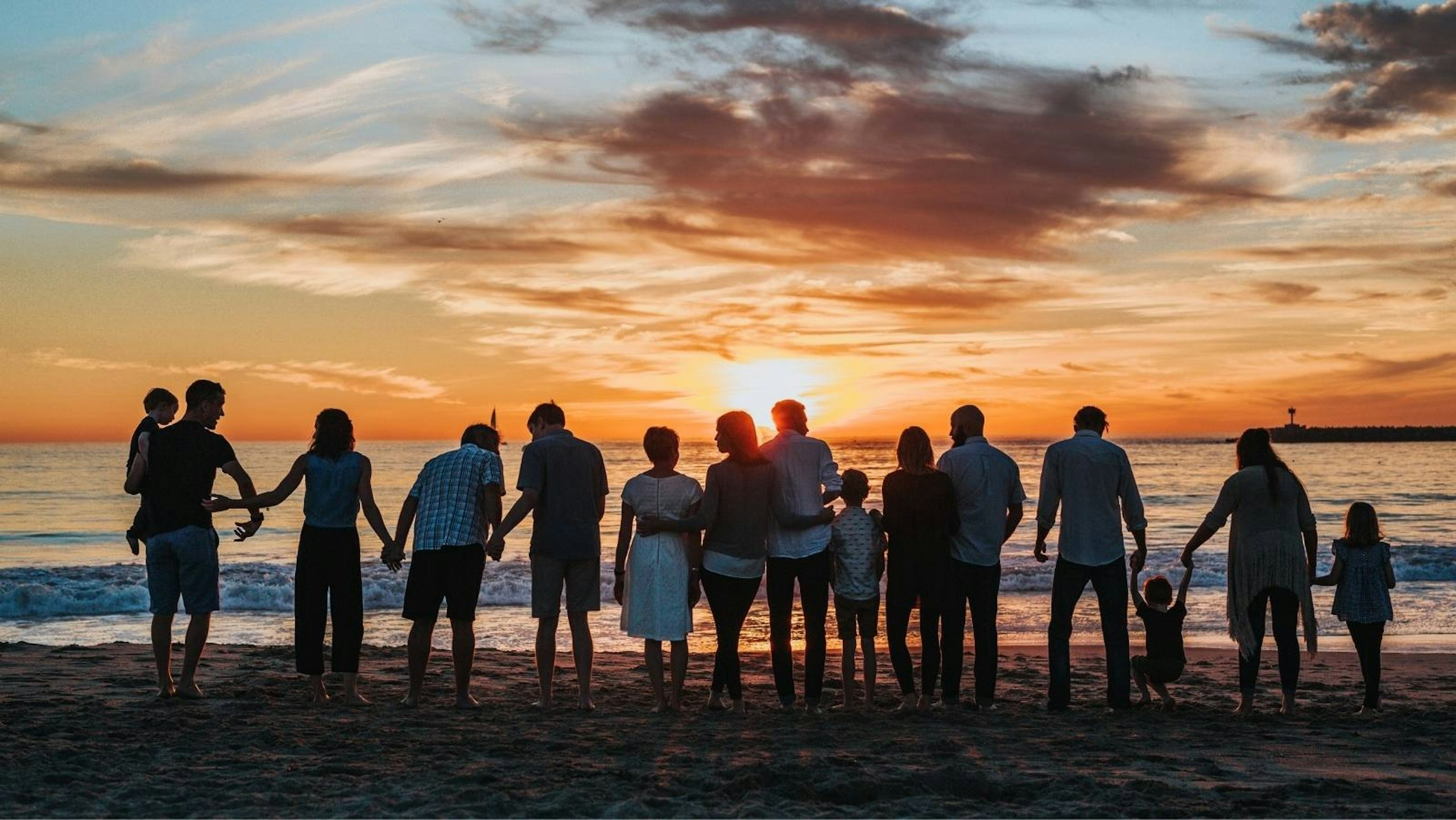 a large group of people on a beach facing the sun on the horizon over the ocean