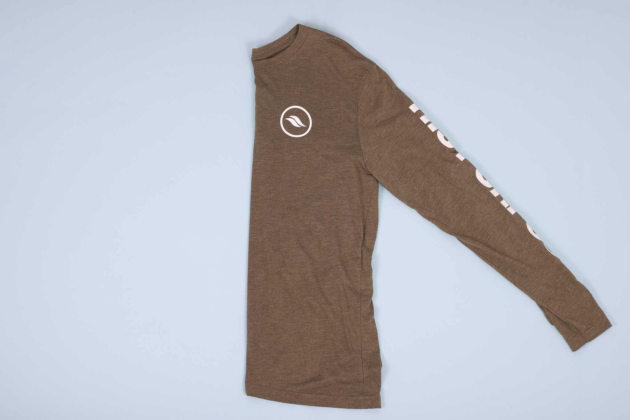 Olive long sleeve shirt with white text on the sleeves folded in half on a light blue background Olive long sleeve shirt with white text on the sleeves folded in half on a light blue background