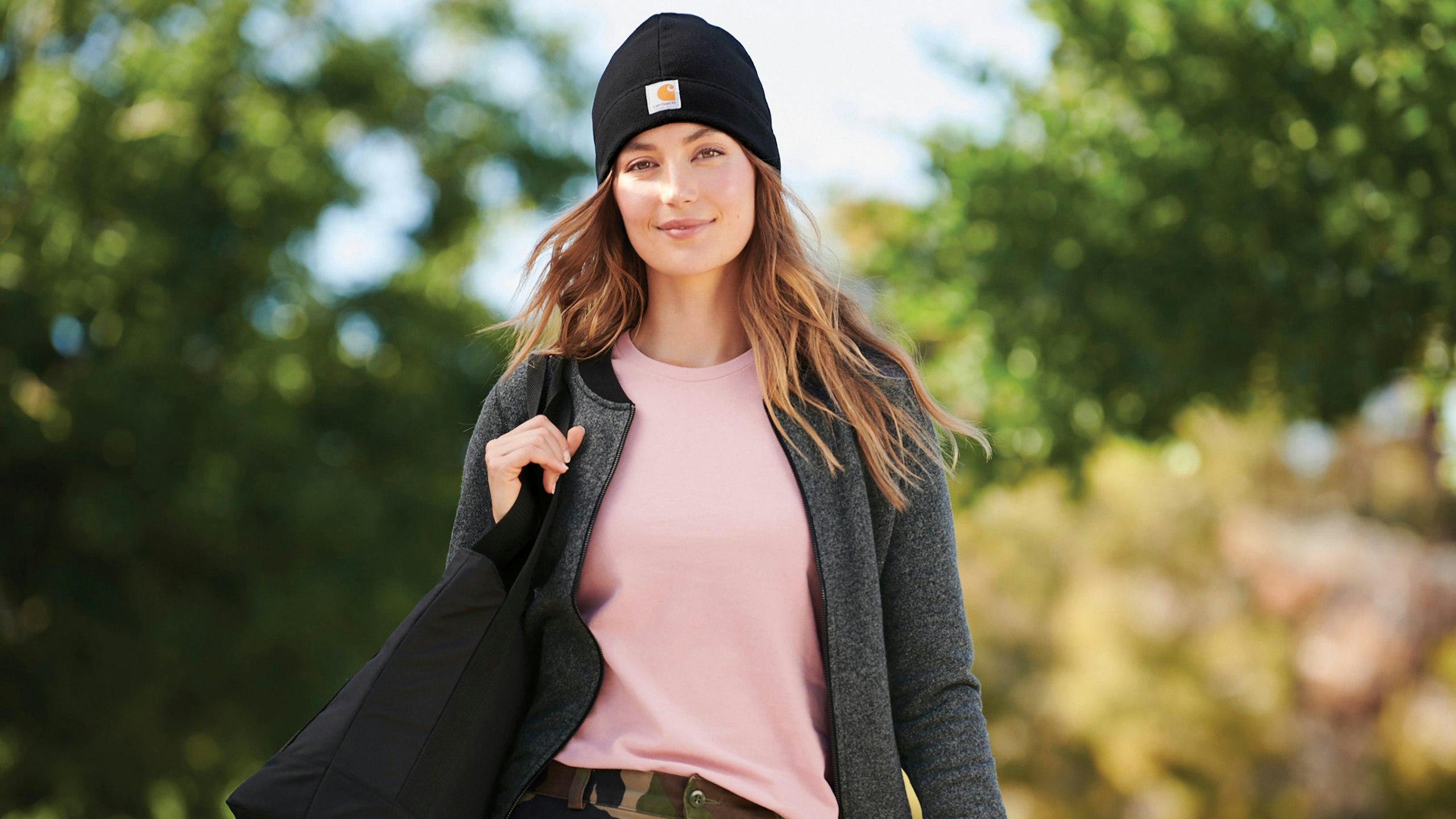 image of a girl wearing a carhartt pink t-shirt, black beanie, and caring a black backpack