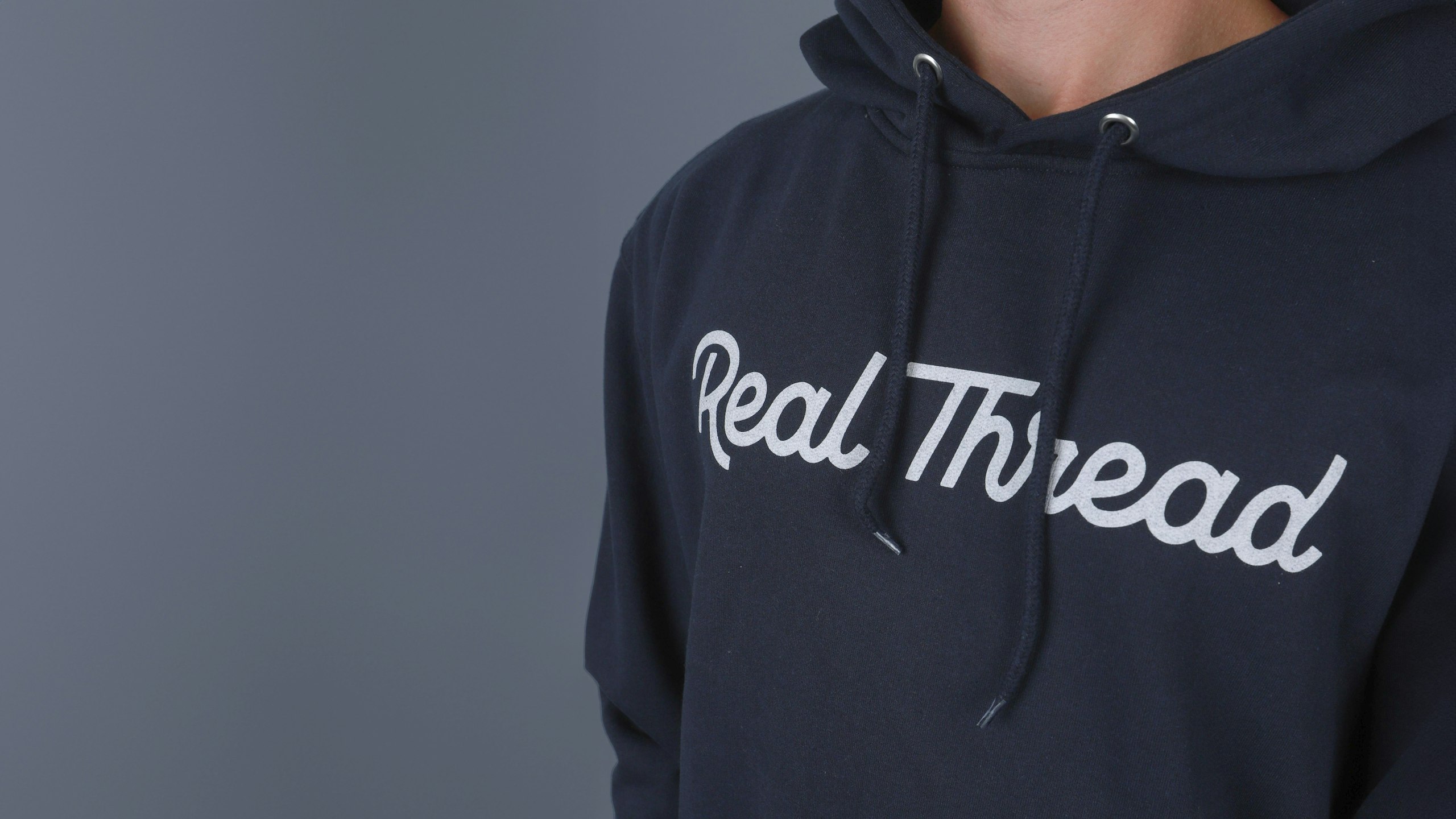someone wearing a navy hoodie with real thread logo print