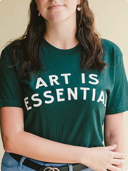 women wearing a green tee with the words art is essential printed in white