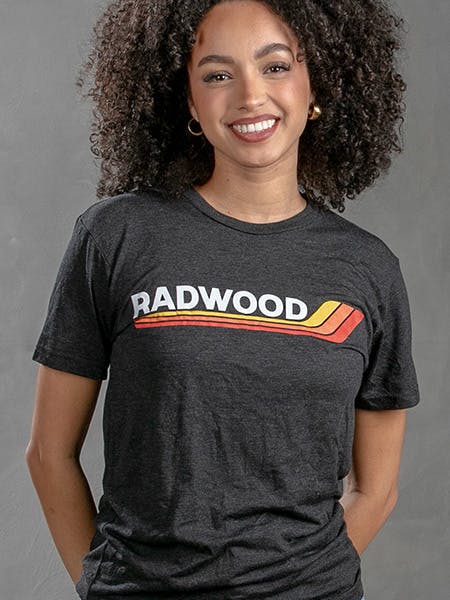 women wearing a dark grey tee with a retro-style logo with yellow, orange, and red lines printed on it