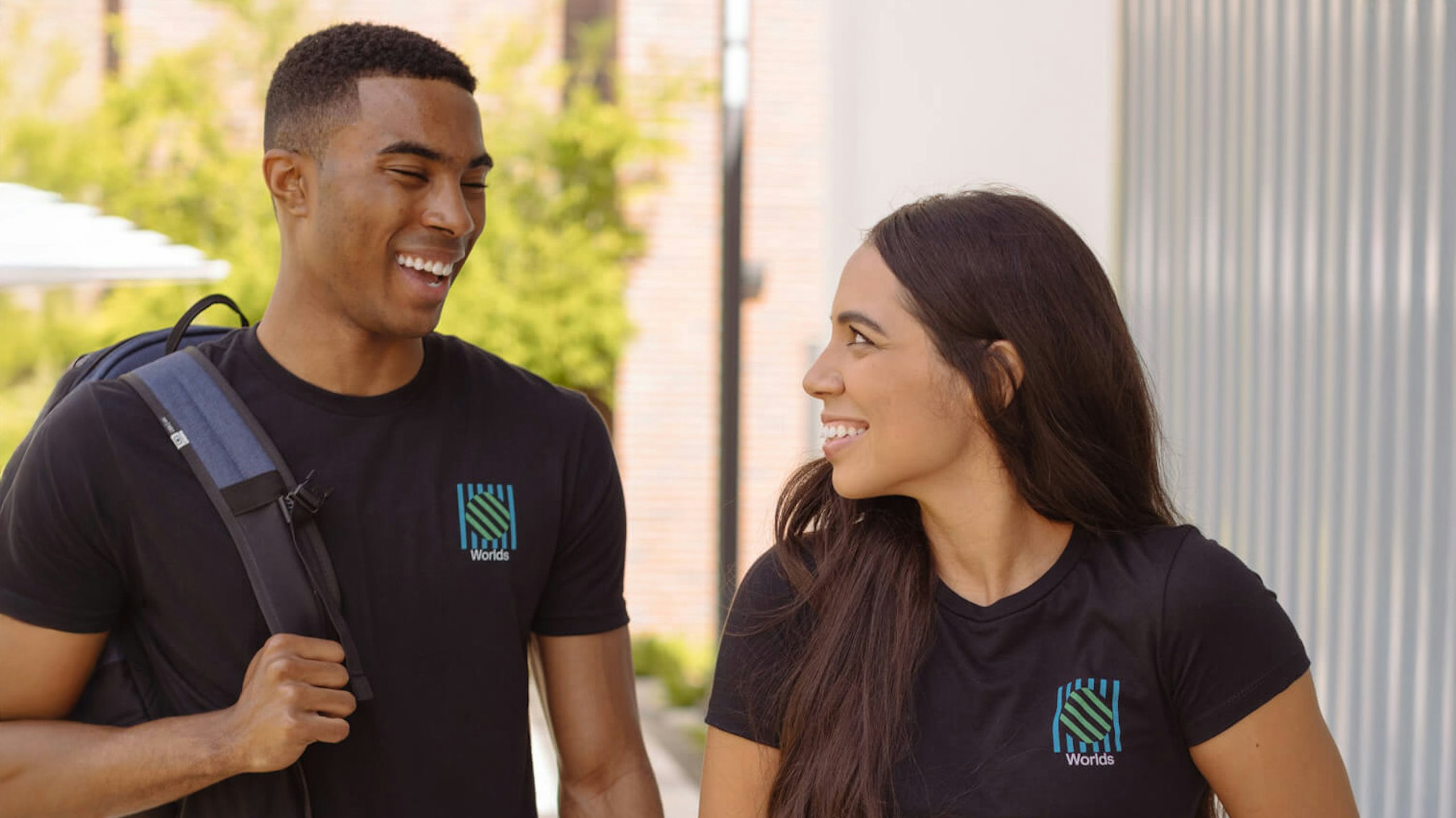 man and women looking at each other wearing black tees with a simple logo on the pocket