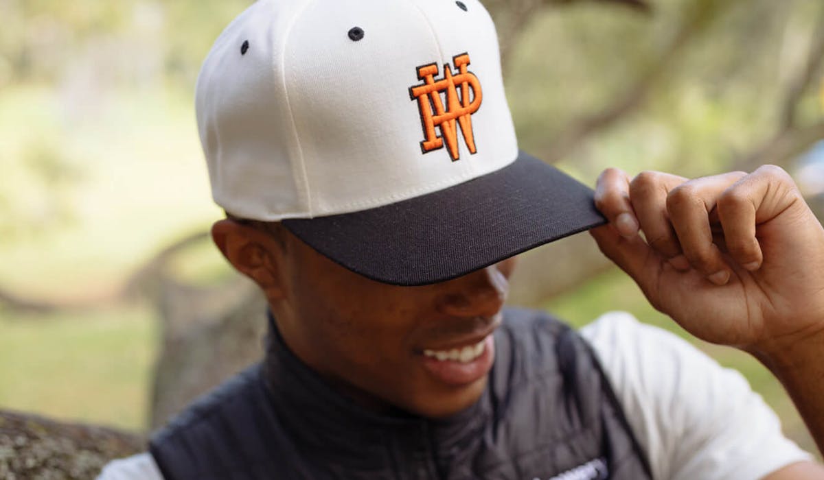 man wearing a white and black hat with a orange p. w. monogram embroidered