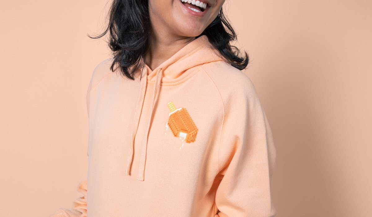 women wearing a peach hoodie with an orange creamsicle embroidered on the top right