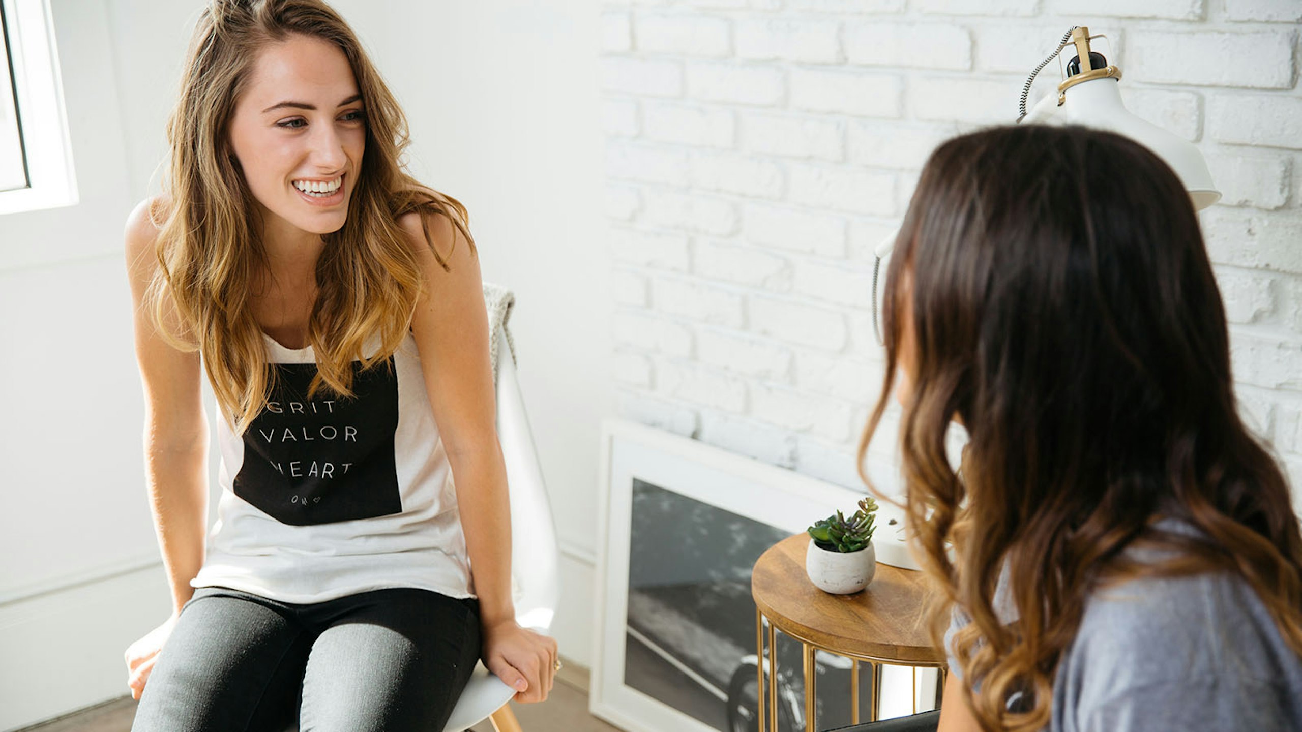 two women talking to each other, one wearing a white tank top