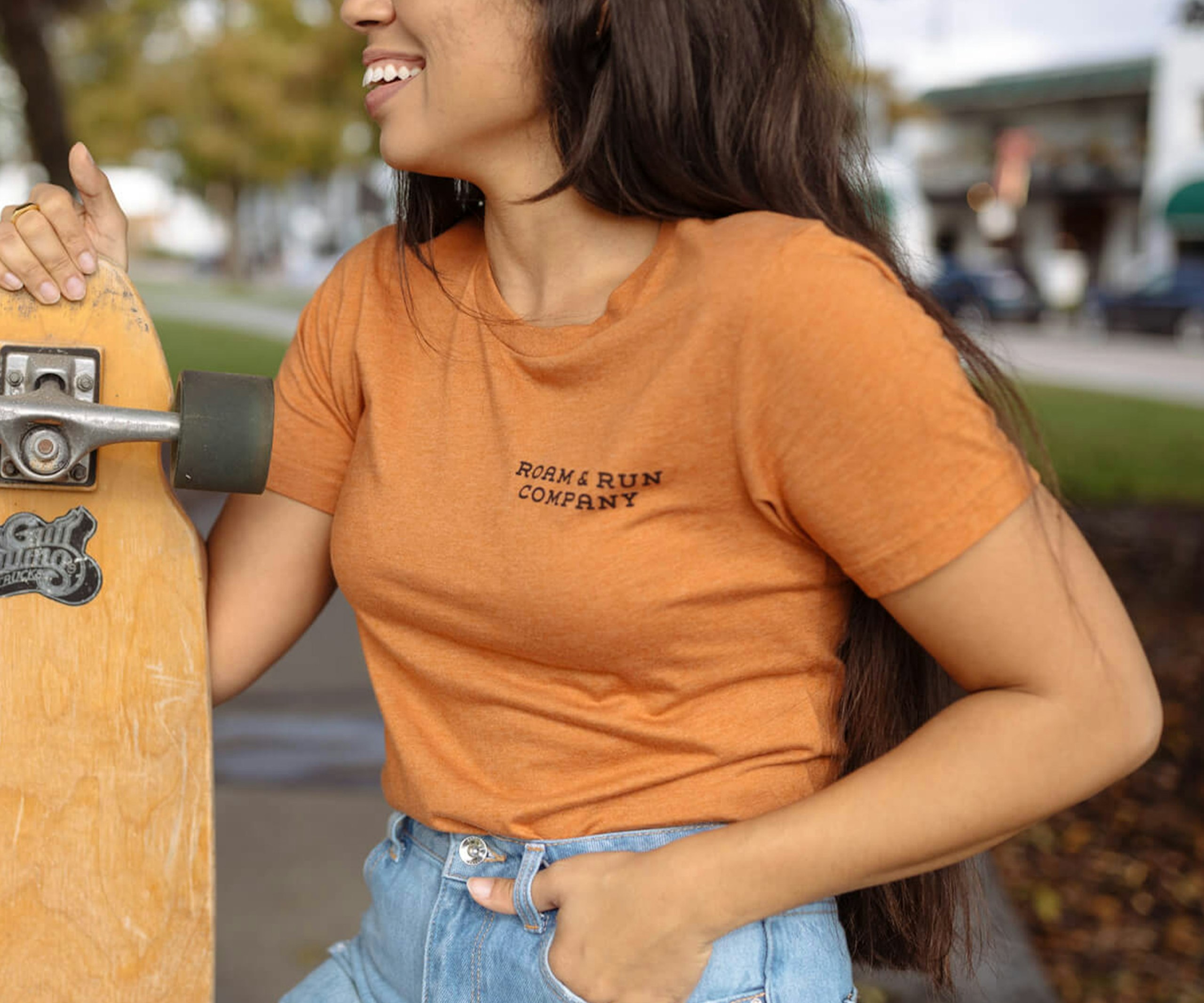 women wearing an orange t-shirt, holding a long board skateboard