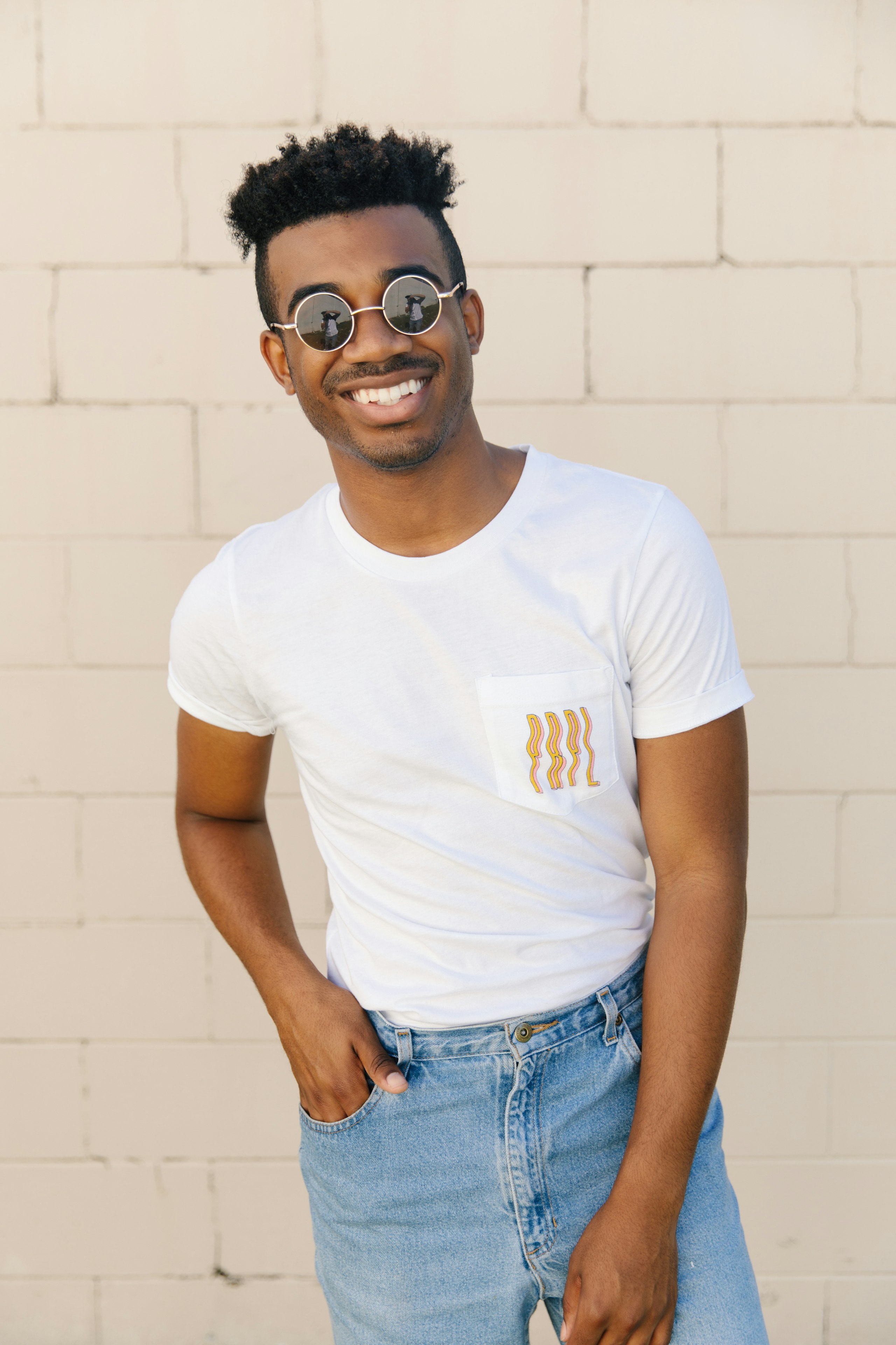 man standing with a white t-shirt in front of a tan cinder block wall