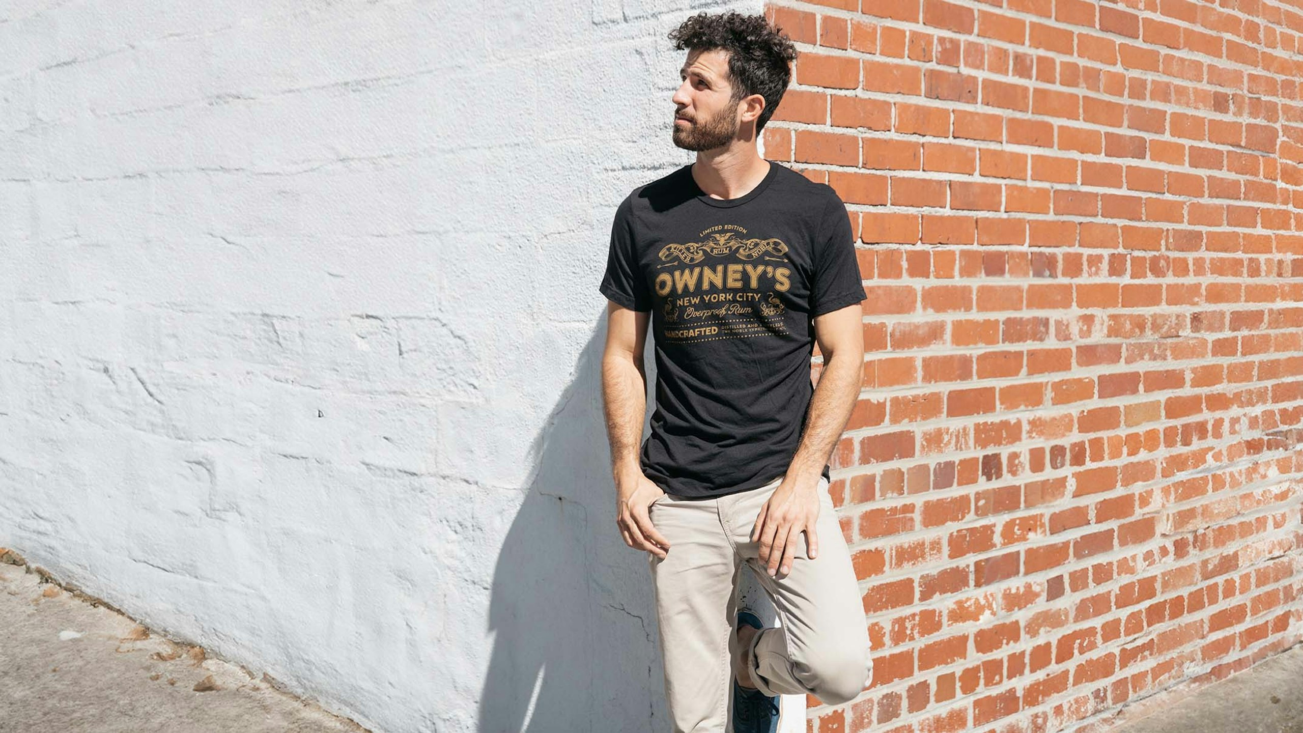 man leaning on a wall wearing a black t-shirt