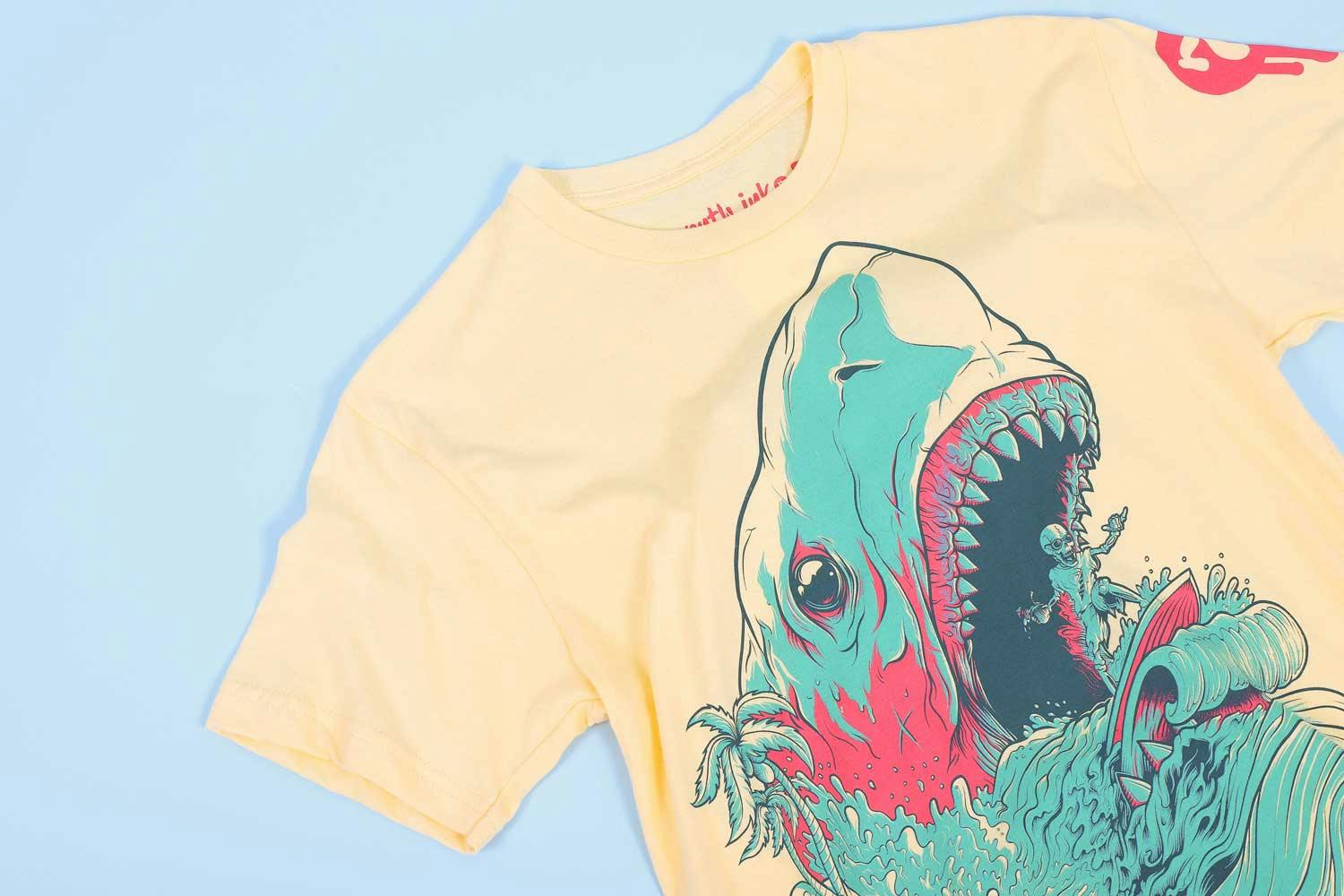 yellow shirt with blue and pink stylized shark and a skeleton riding a surfboard out of its mouth yellow shirt with blue and pink stylized shark and a skeleton riding a surfboard out of its mouth