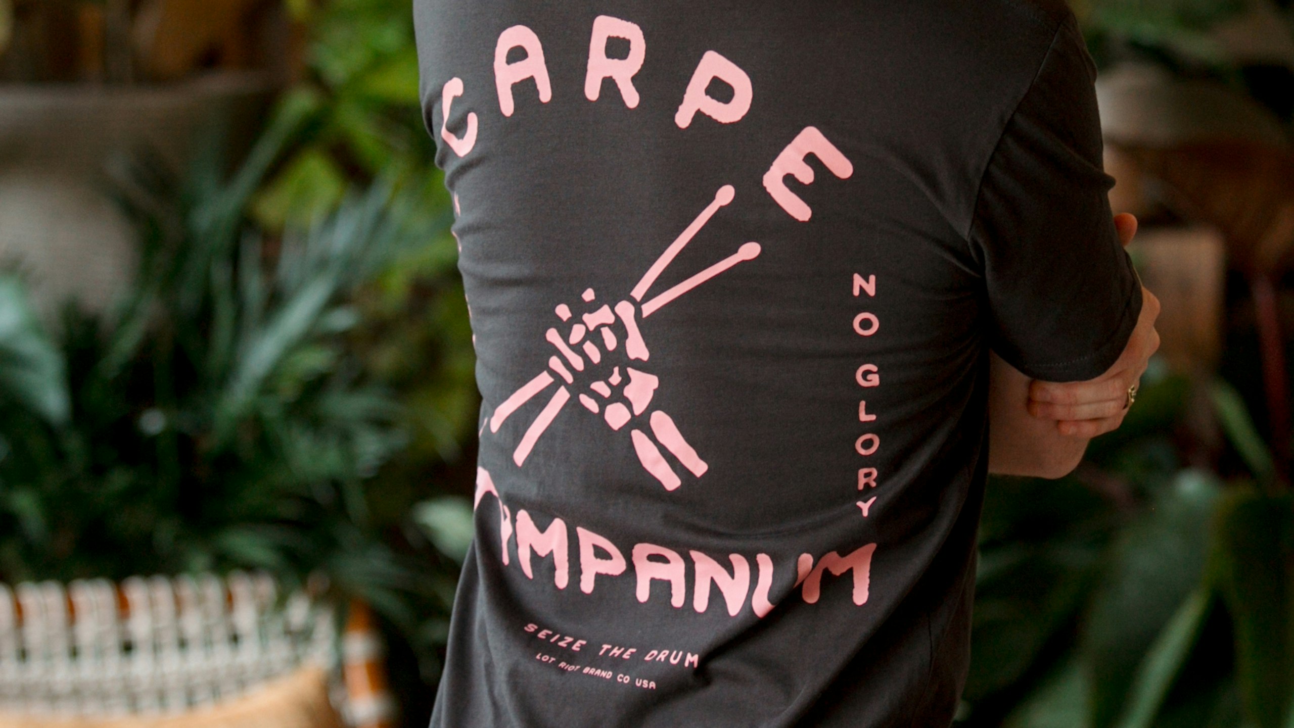 close up of a man wearing a black t-shirt with pink drum sticks printed on the back
