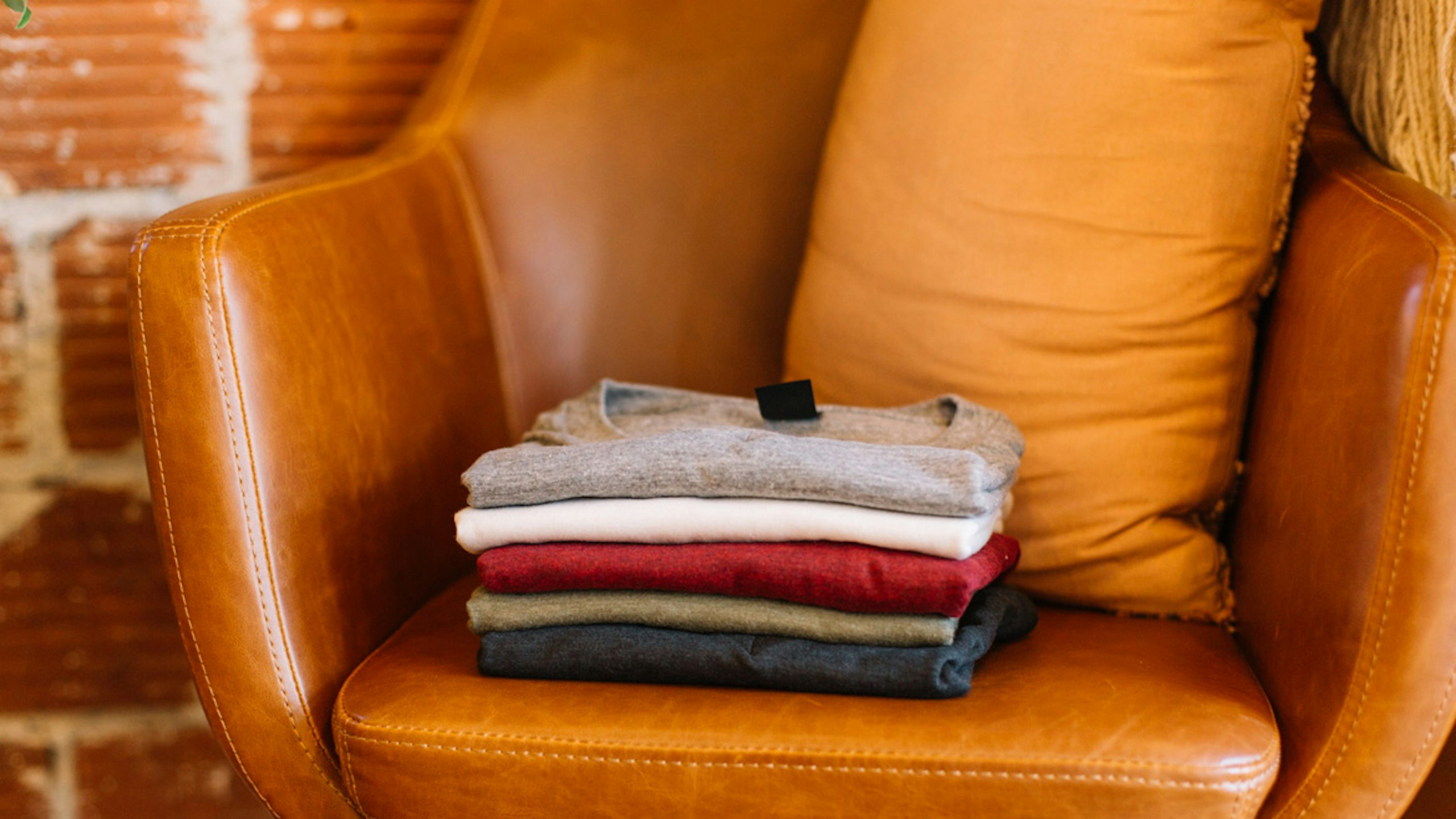 a stack of folded allmade tees on a orange leather chair