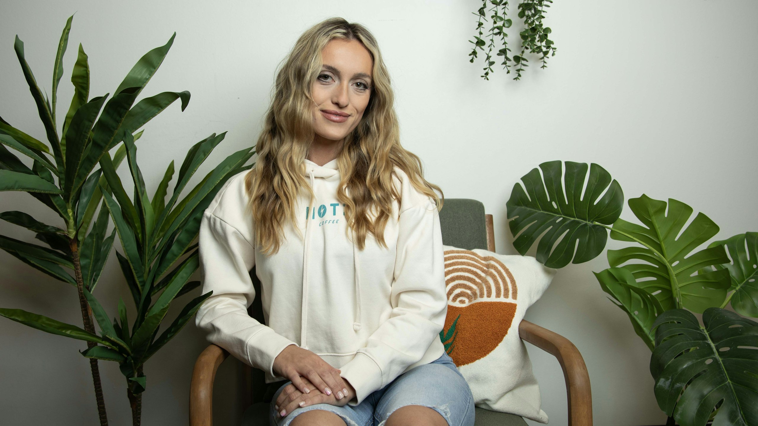 Women sitting wearing a white hoodie with blue wordmark printed on it
