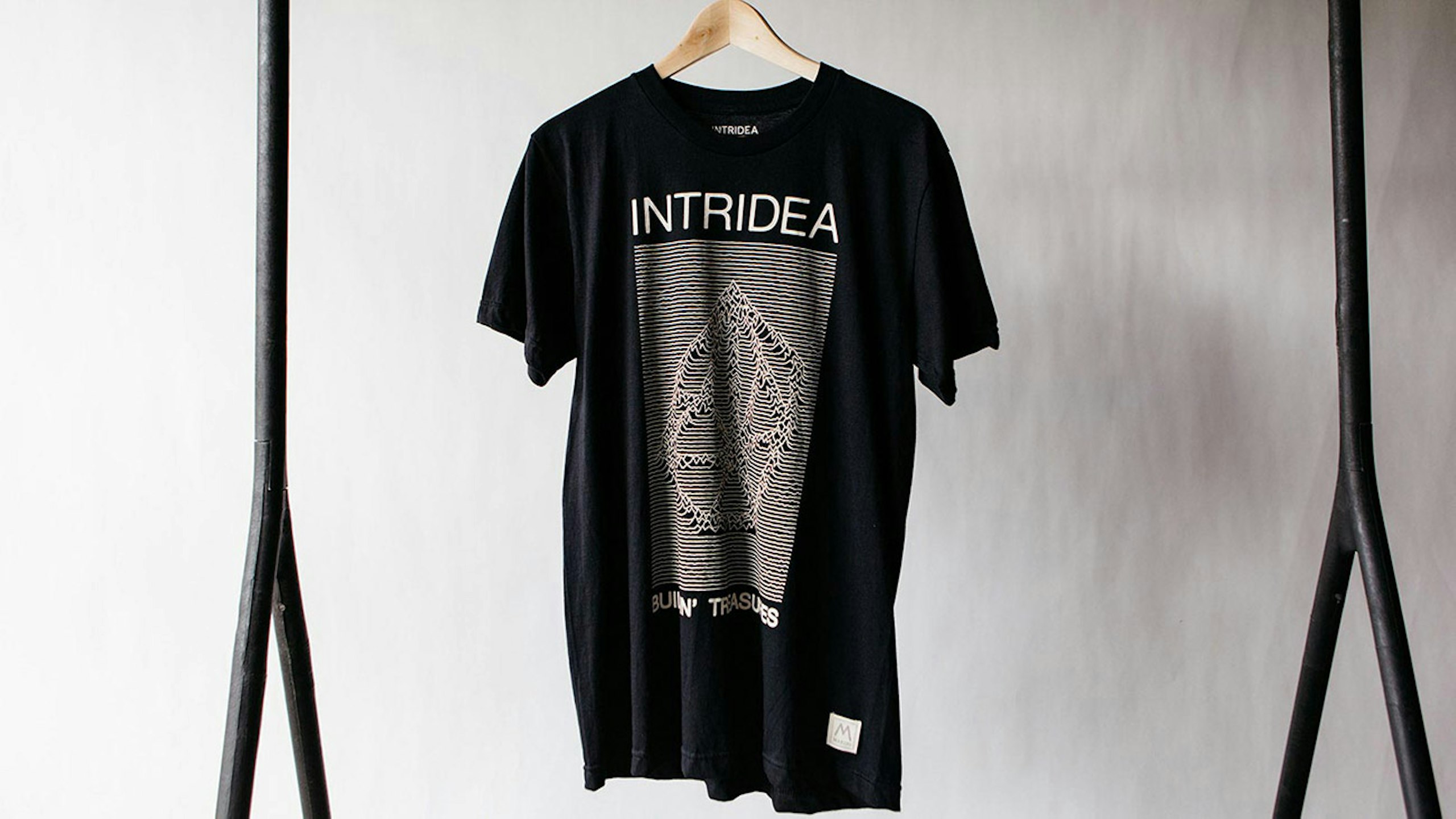 A black t-shirt with a white printed design hangs in front of a gray backdrop