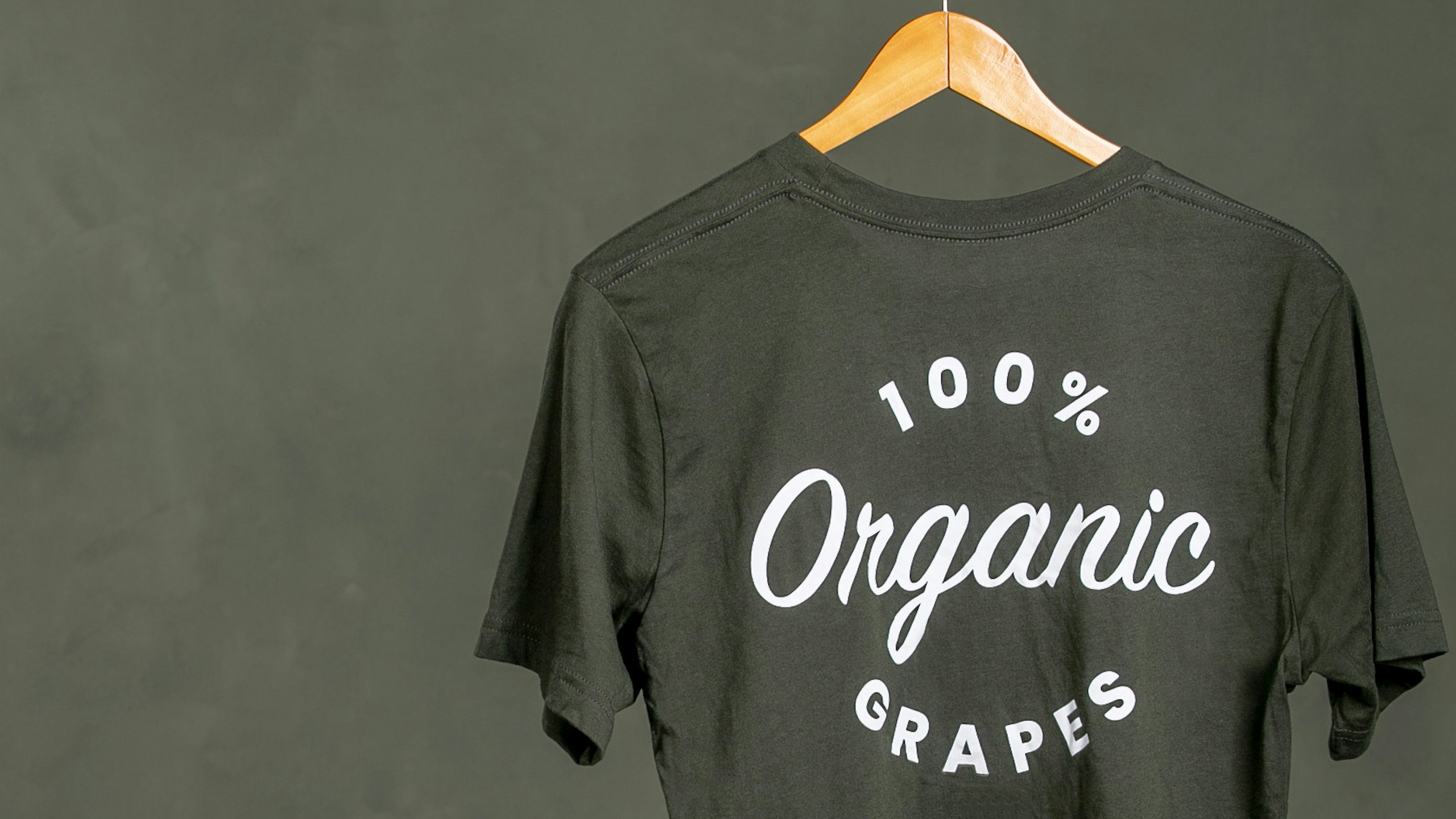 dark olive green t-shirt with the words 100 percent organic grapes hanging on a hanger