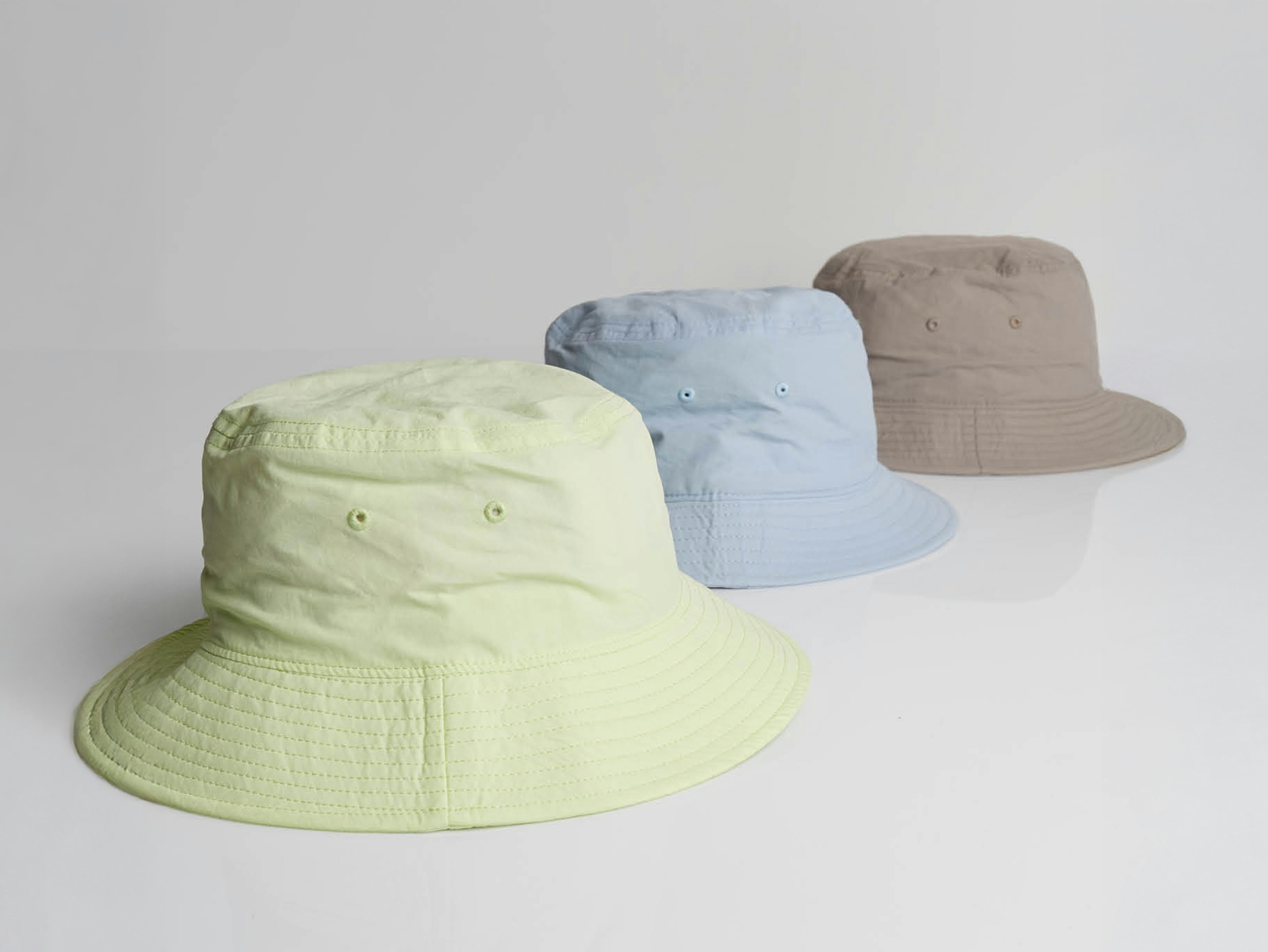 three bucket hats, lime, powder blue, and mushroom brown, on a white background