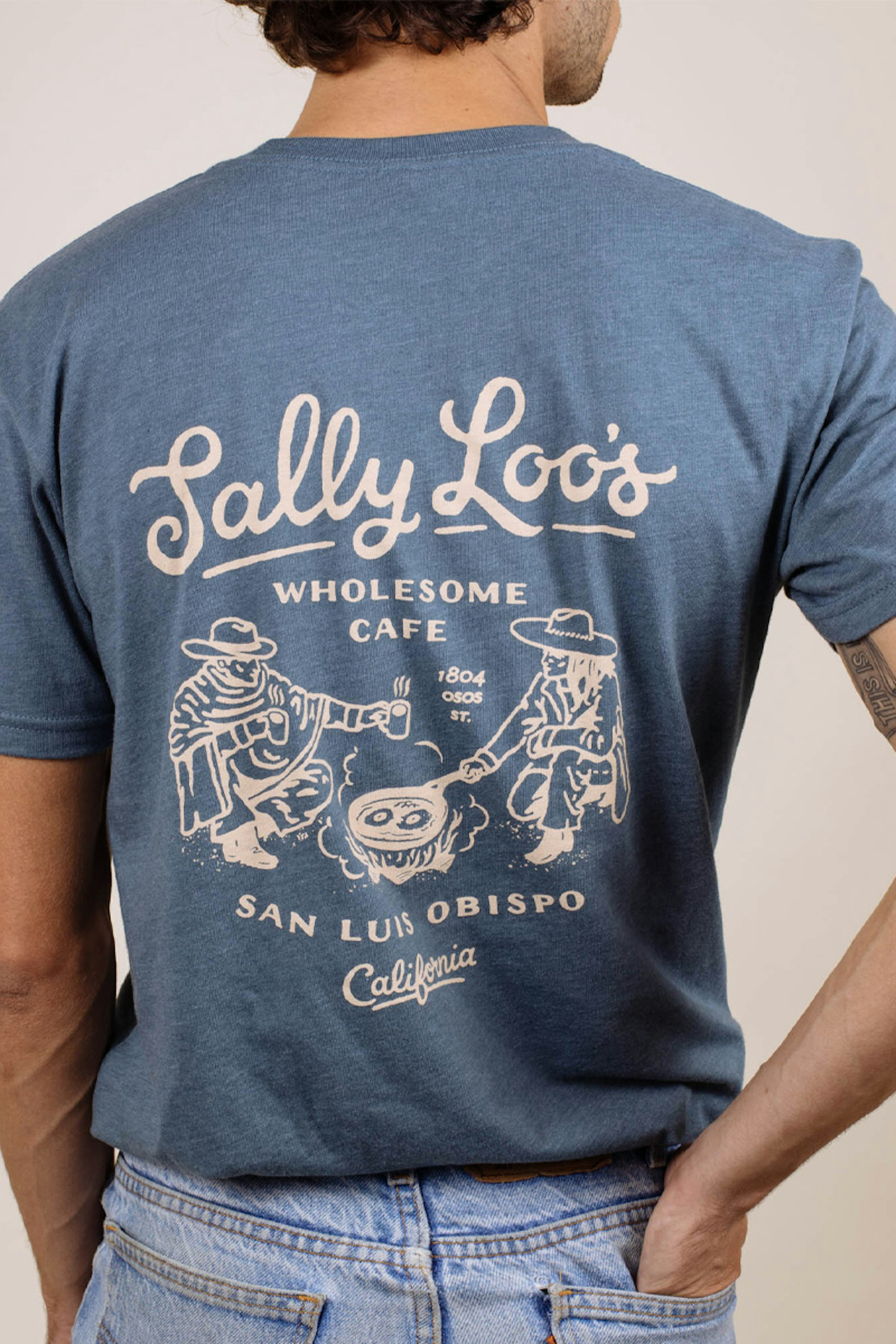 the back of a man wearing a slate blue t-shirt with a cowboy and camp fire illustration