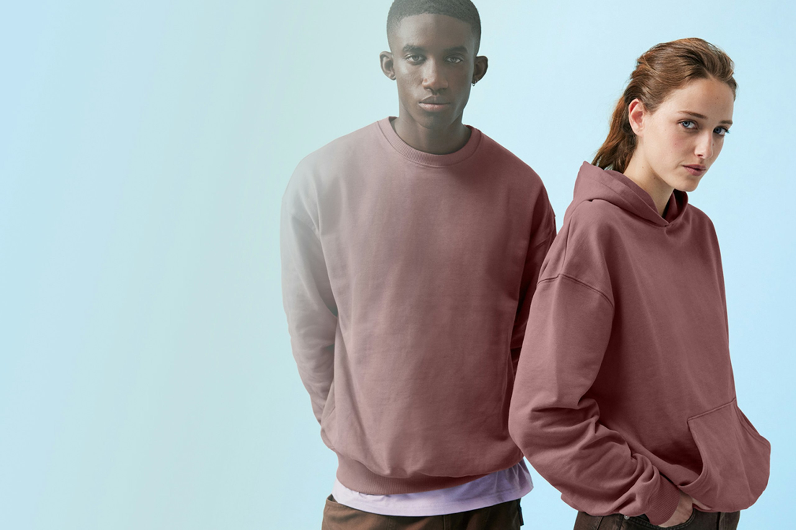two people wearing dark pink sweatshirts and hoodies in front of a blue background