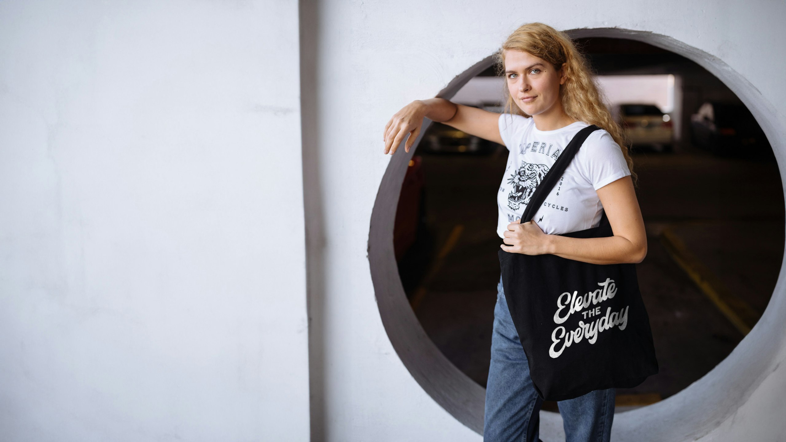 women wearing a white shirt and holding a black tote bag with the words "elevate the everyday" printed on it