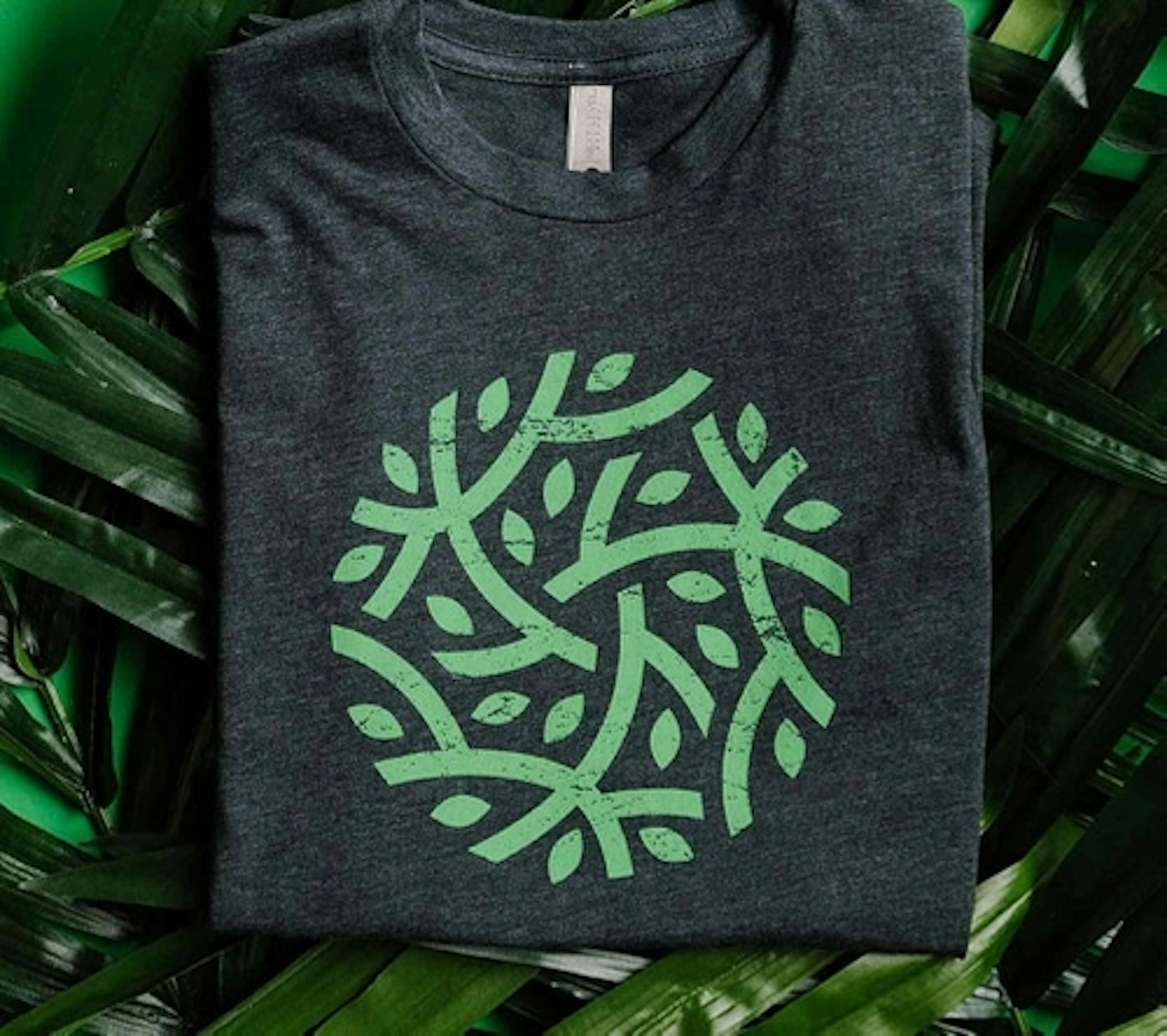 Green branch and leaf design inside of circle printed on a dark green shirt