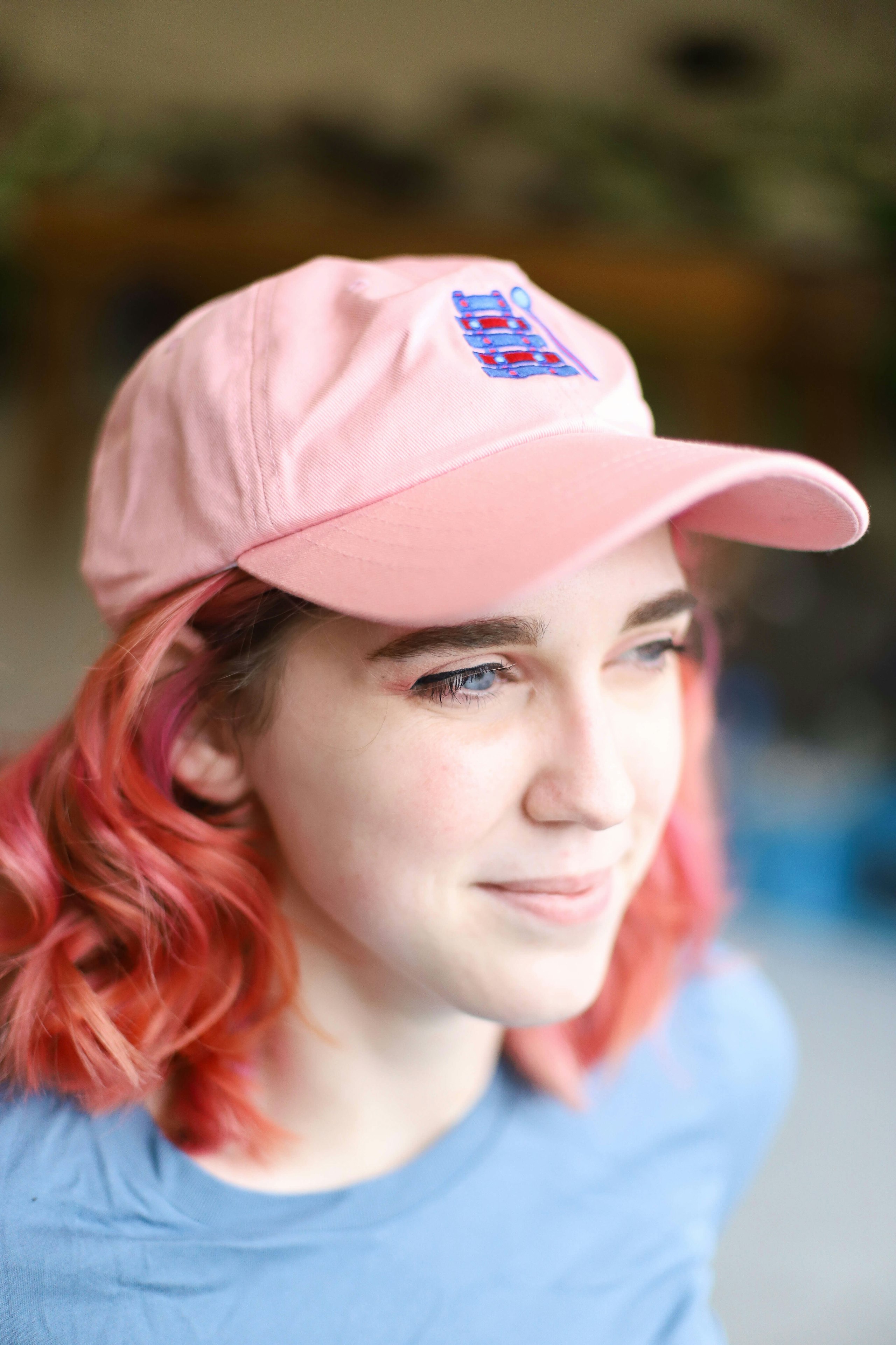 A girl with pink hair wears a pink hat with custom embroidered xylophone.