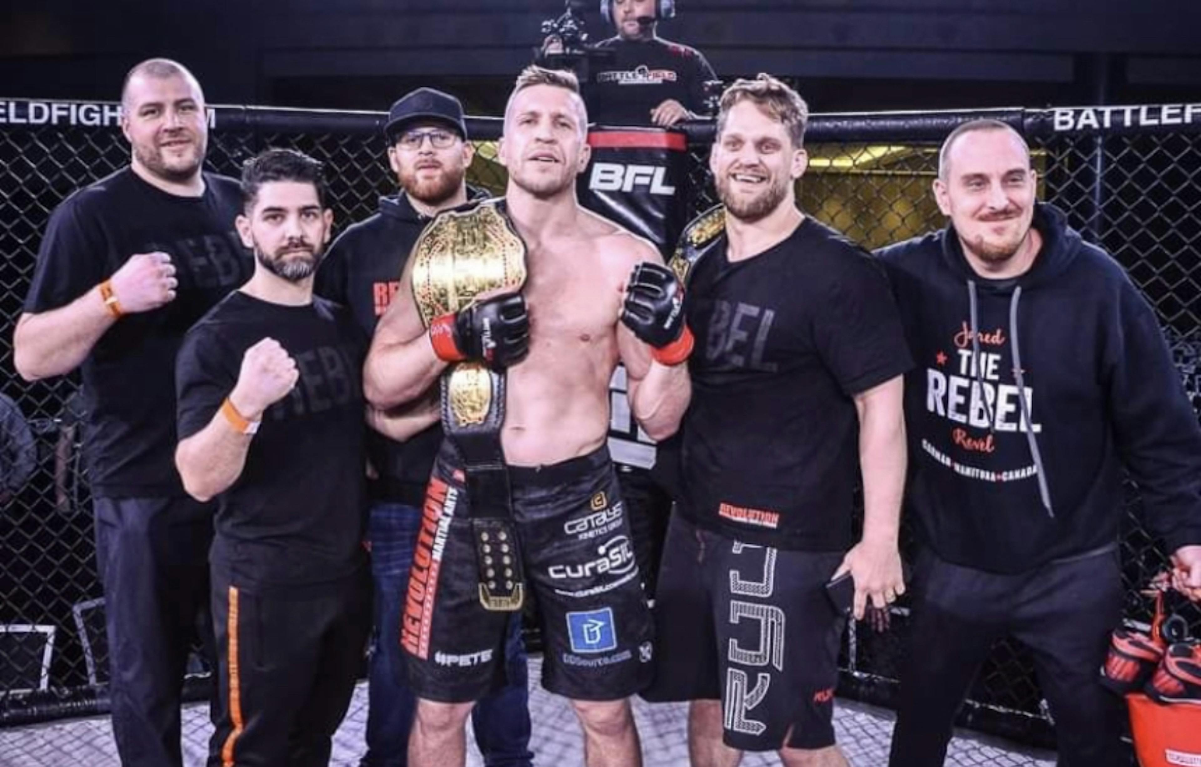 Jared and Brad celebrate Jared's victory inside the octagon as they pose for a picture with their team