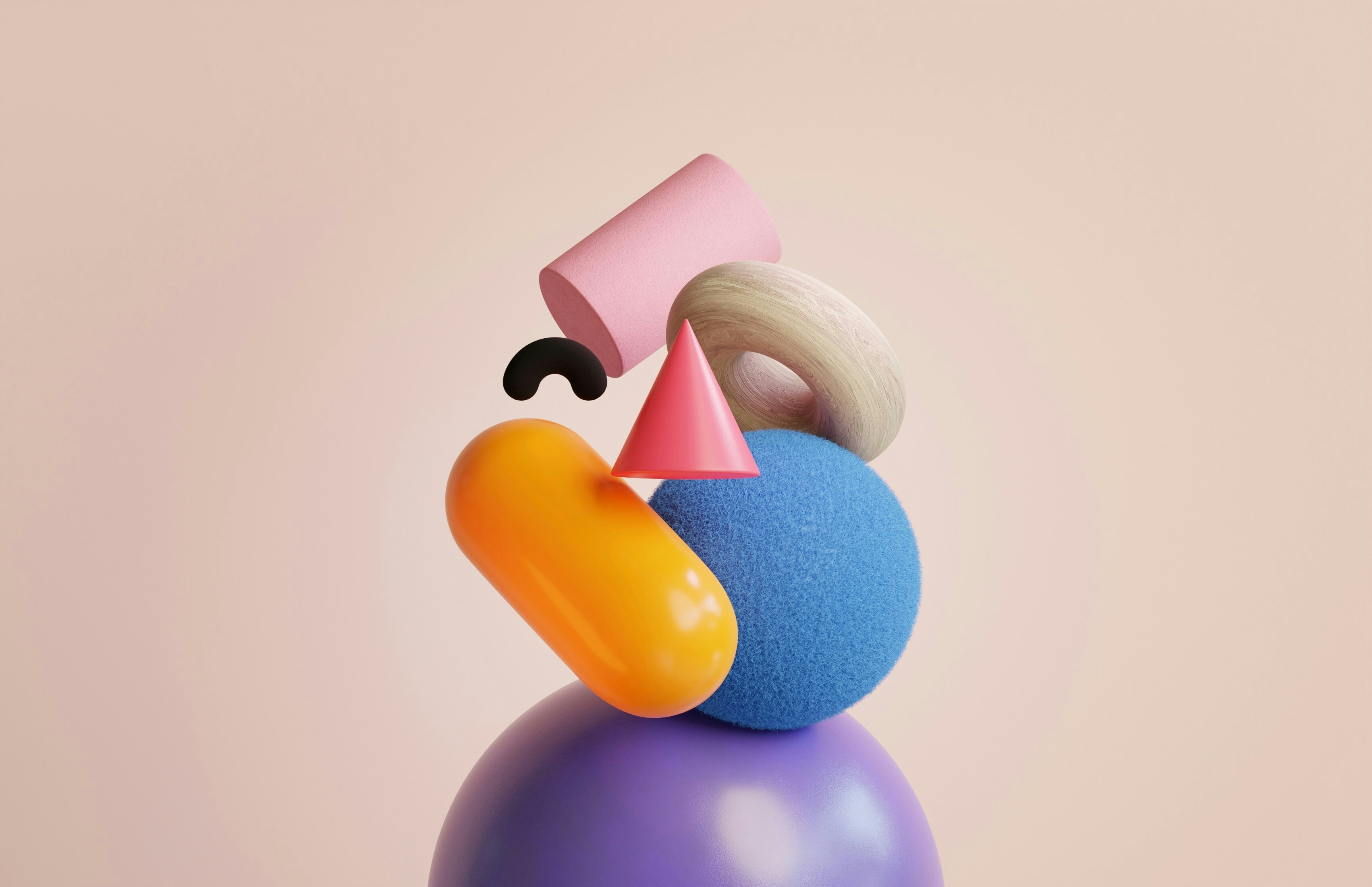 The image features a balanced arrangement of colorful, abstract 3D shapes against a soft, light pink background. The shapes include a large purple sphere at the bottom, a blue textured sphere above it, a cylindrical pink shape, an orange capsule-like shape, a beige torus, a pink cone, and a small black curved shape. The objects are stacked in an artful and visually intriguing manner, creating a sense of playful balance and composition.
