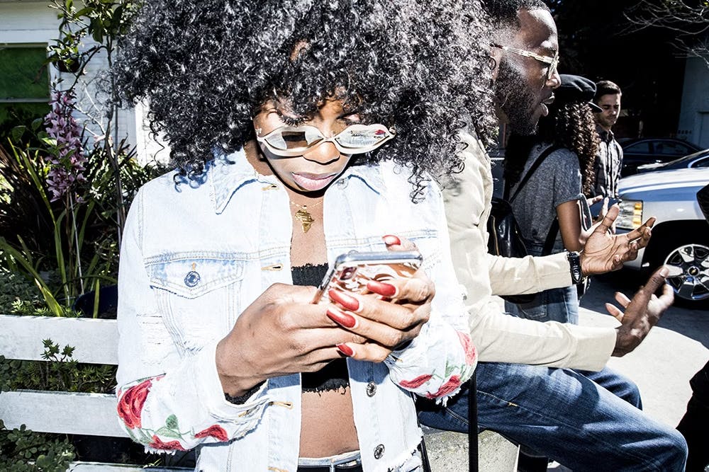 Person with an afro, sunglasses, and red nail polish looking at their phone