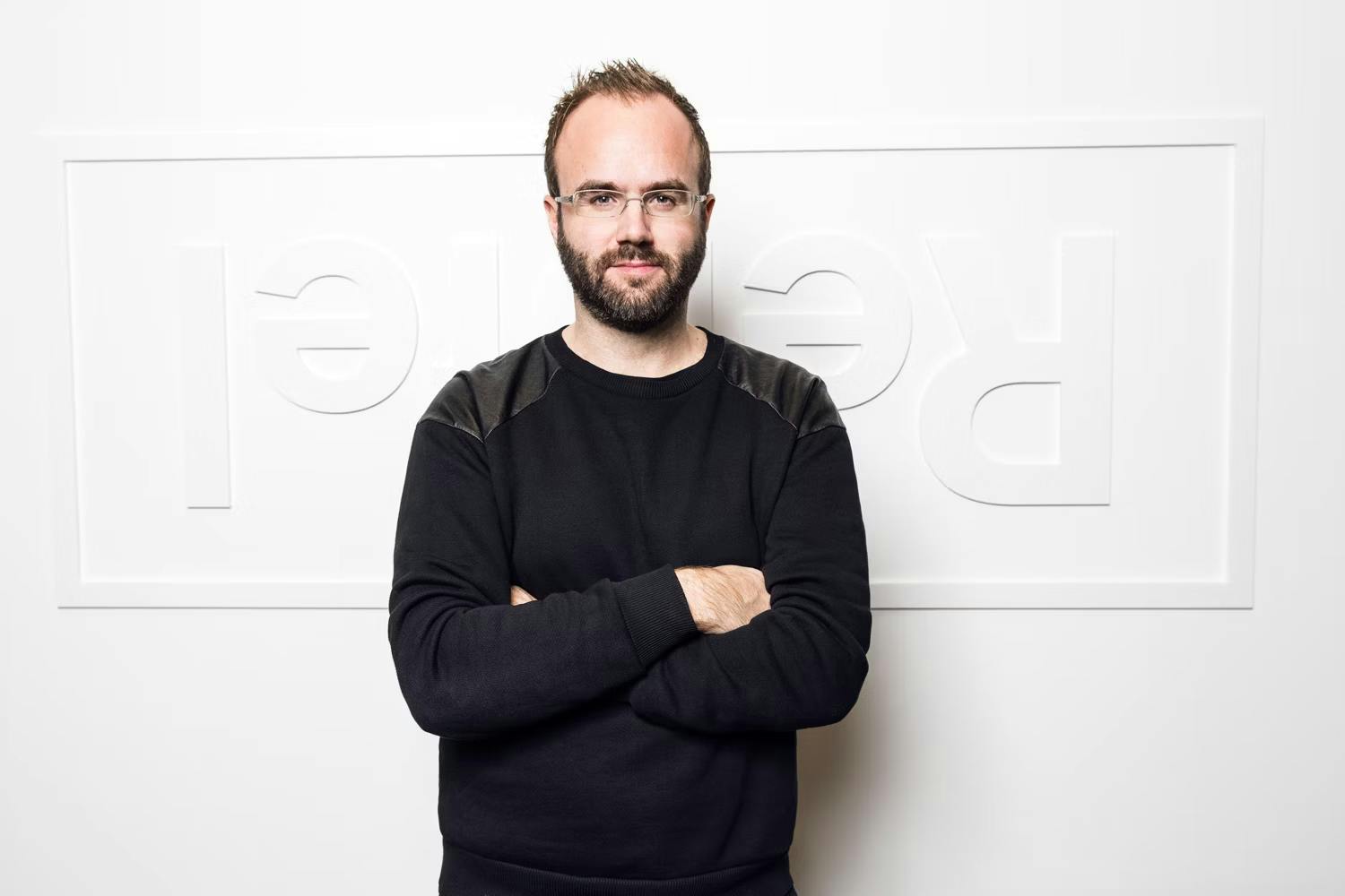 Magnus Larsson, a white man wearing a black sweater and glasses, standing in front of the Rebtel logo against a white wall