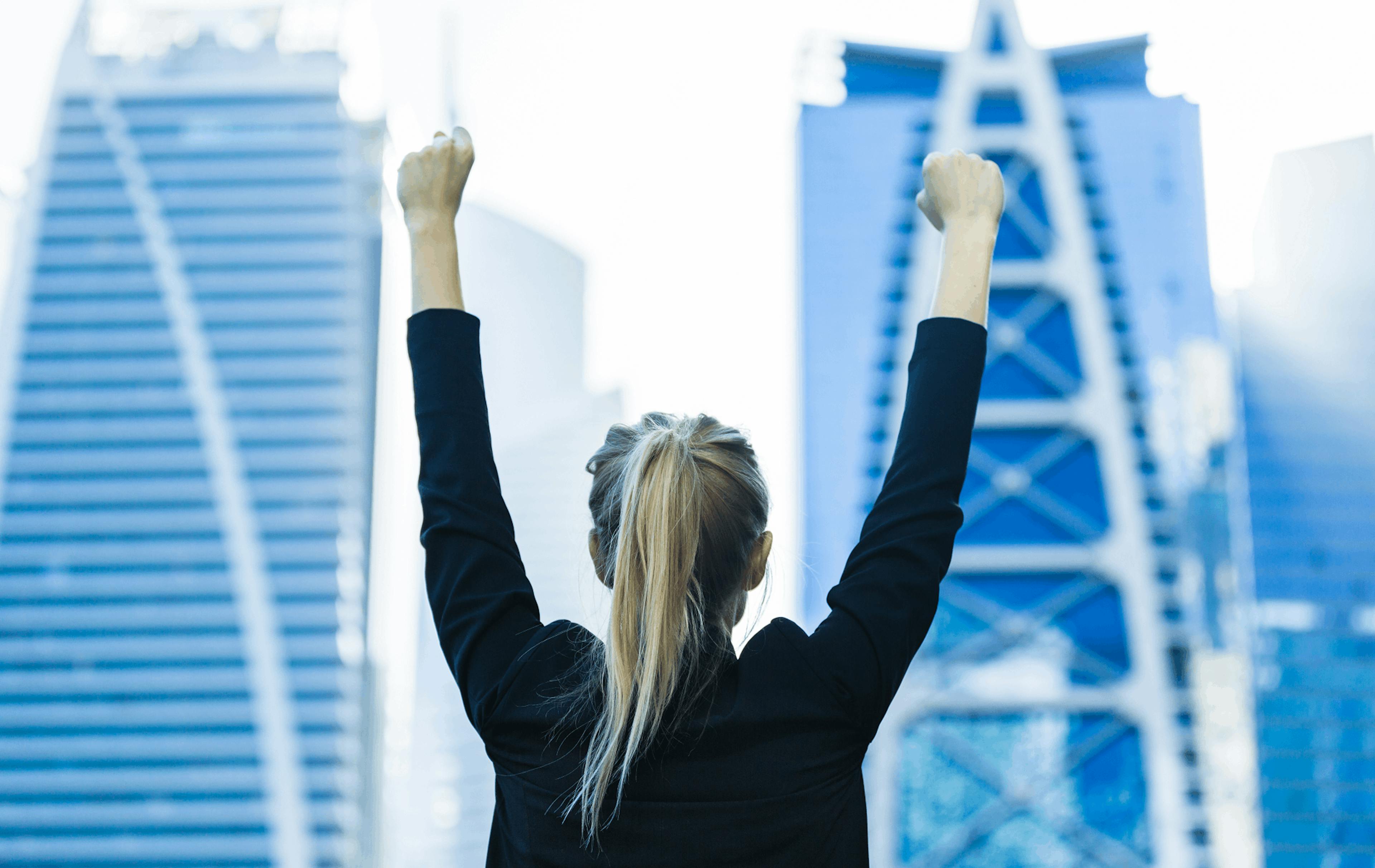 a woman raising her hands while facing huge buildings