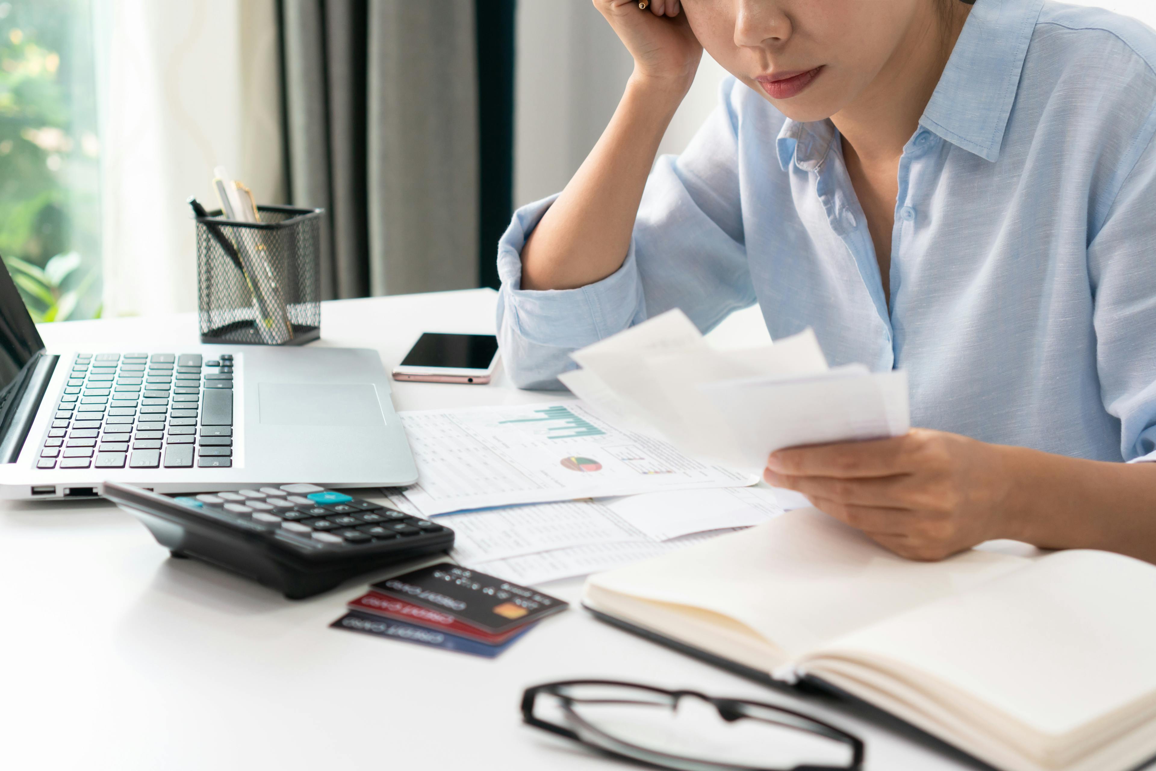 a close-up stressed Asian woman checking bills, taxes, and bank account balance