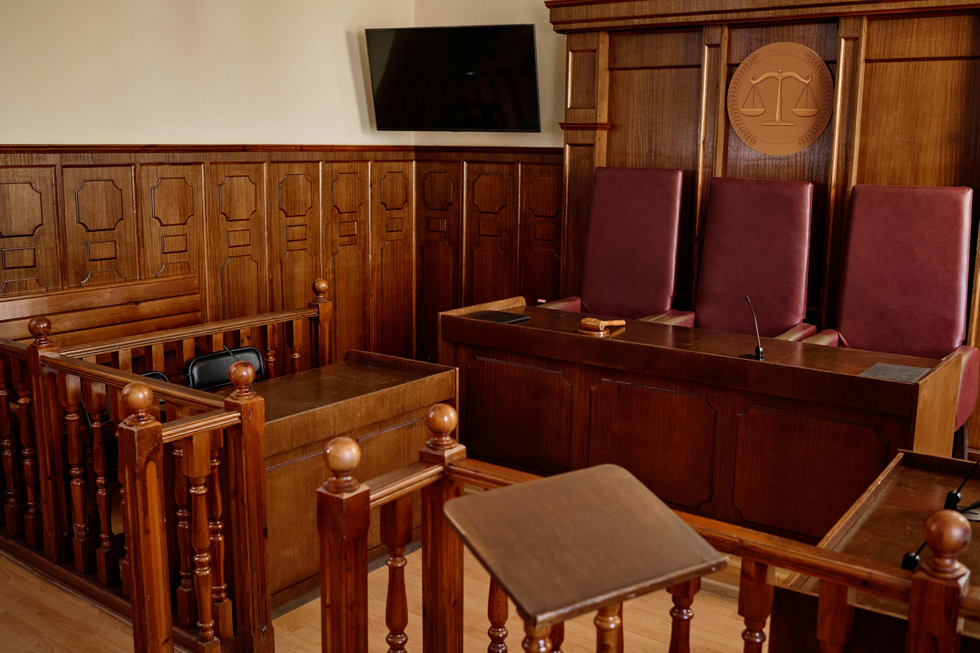 spacious courtroom with wooden desks, railings, and leather chairs