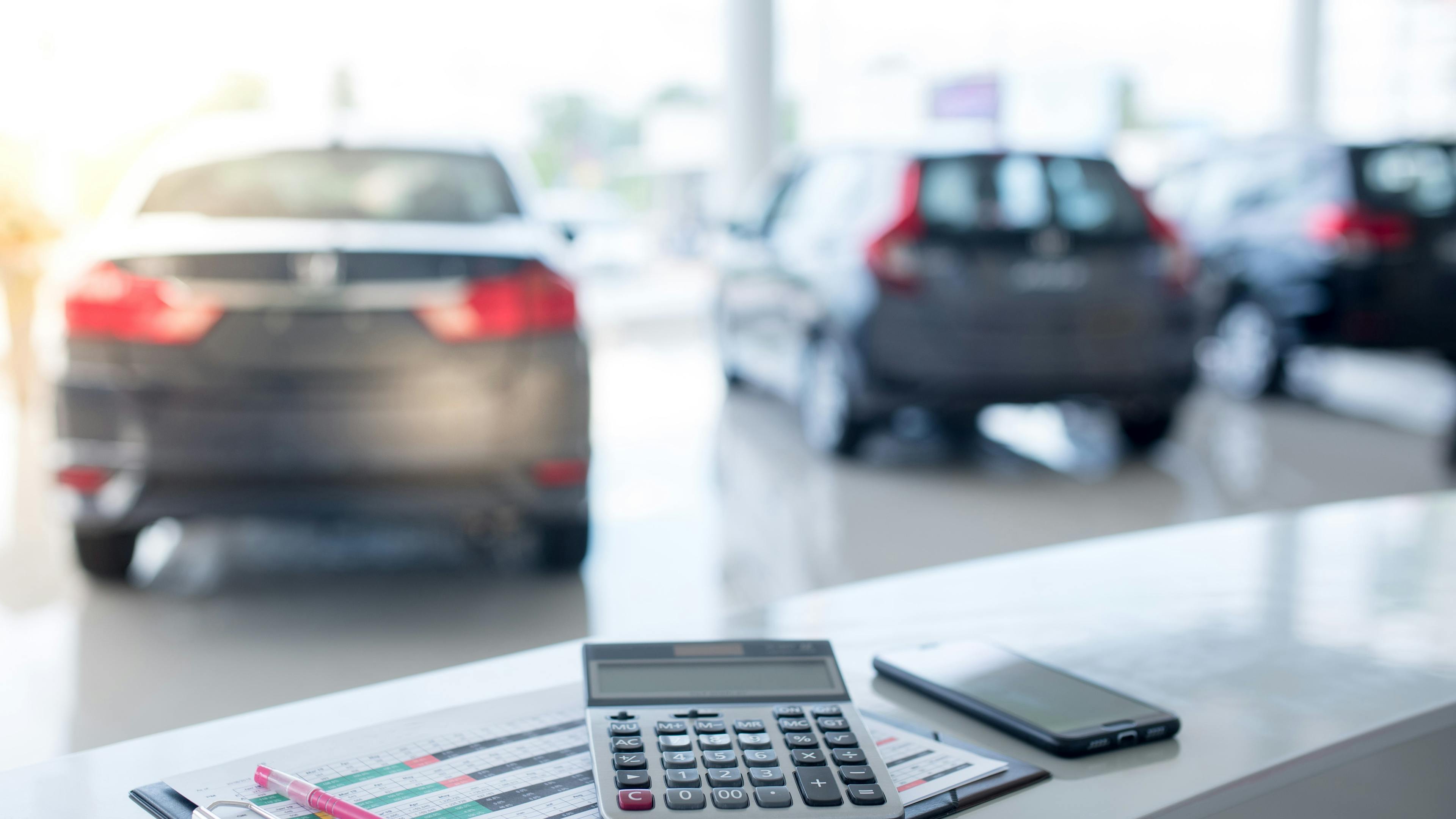Calculator on desk in dealership with cars in background.