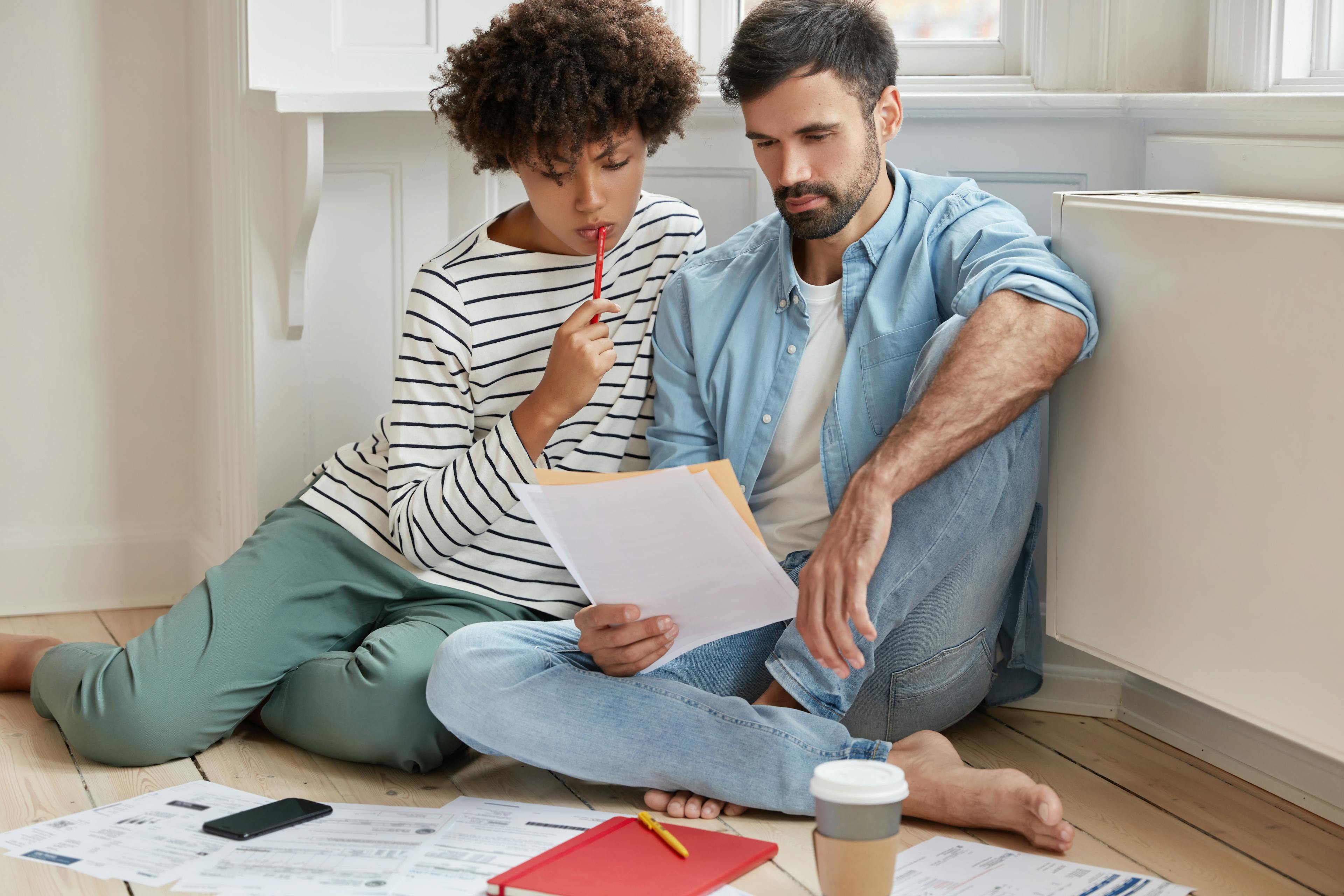 Couple sits on floor intently reviewing documents together