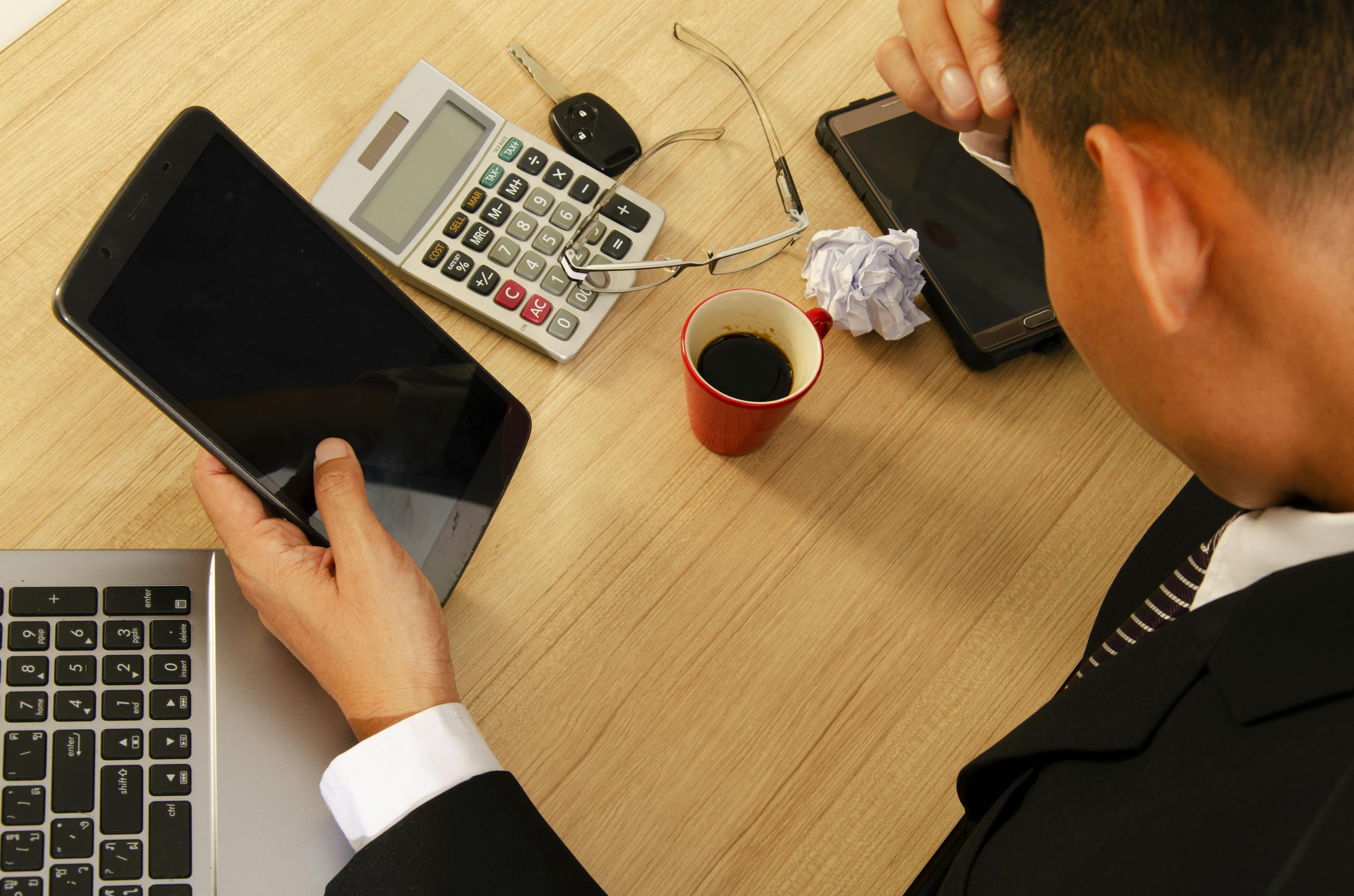A man stressed on his car finance refund with tablet, calculator and laptop on the table.
