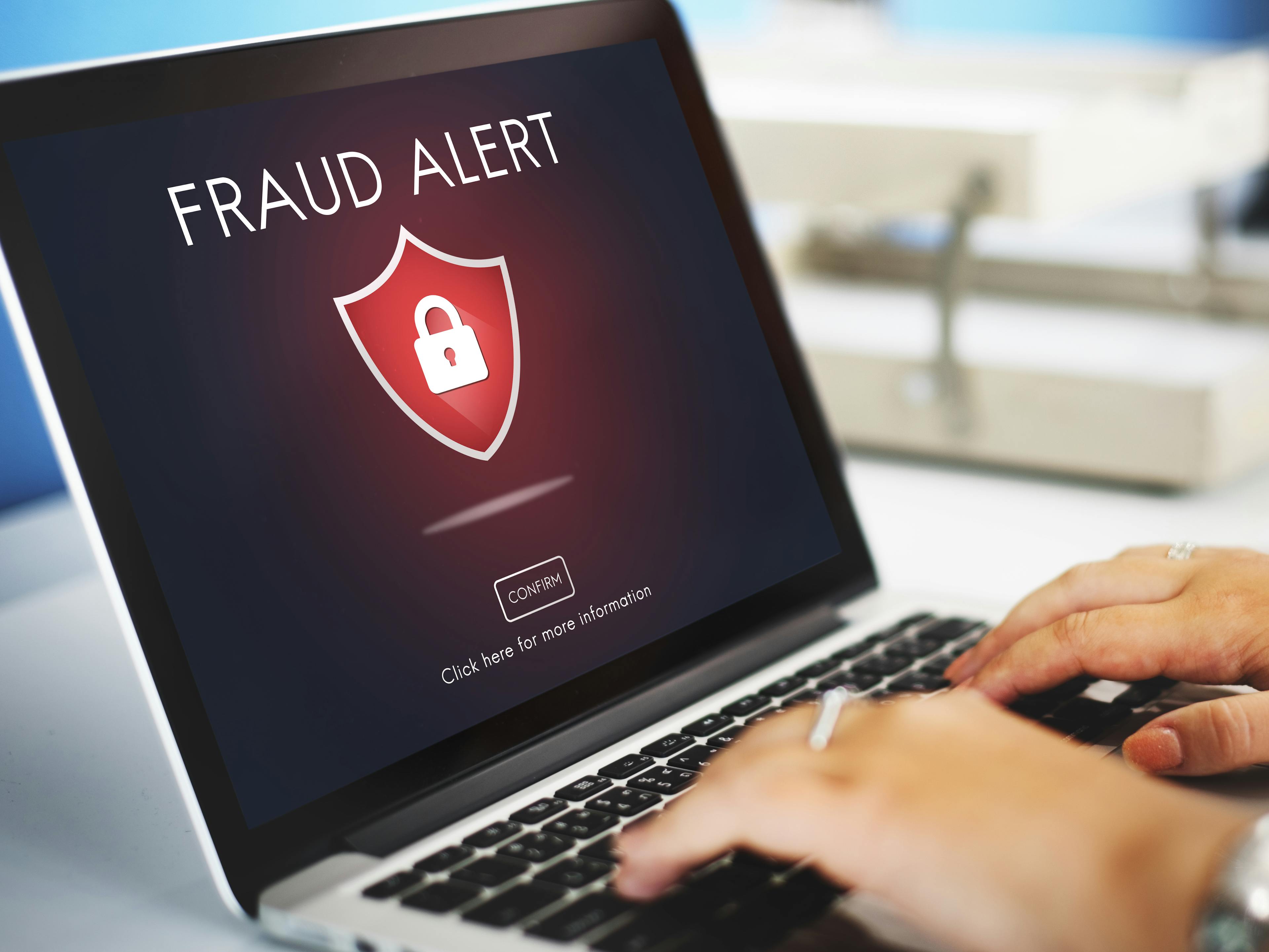 hands typing on a laptop keyboard with the screen showing "fraud alert"