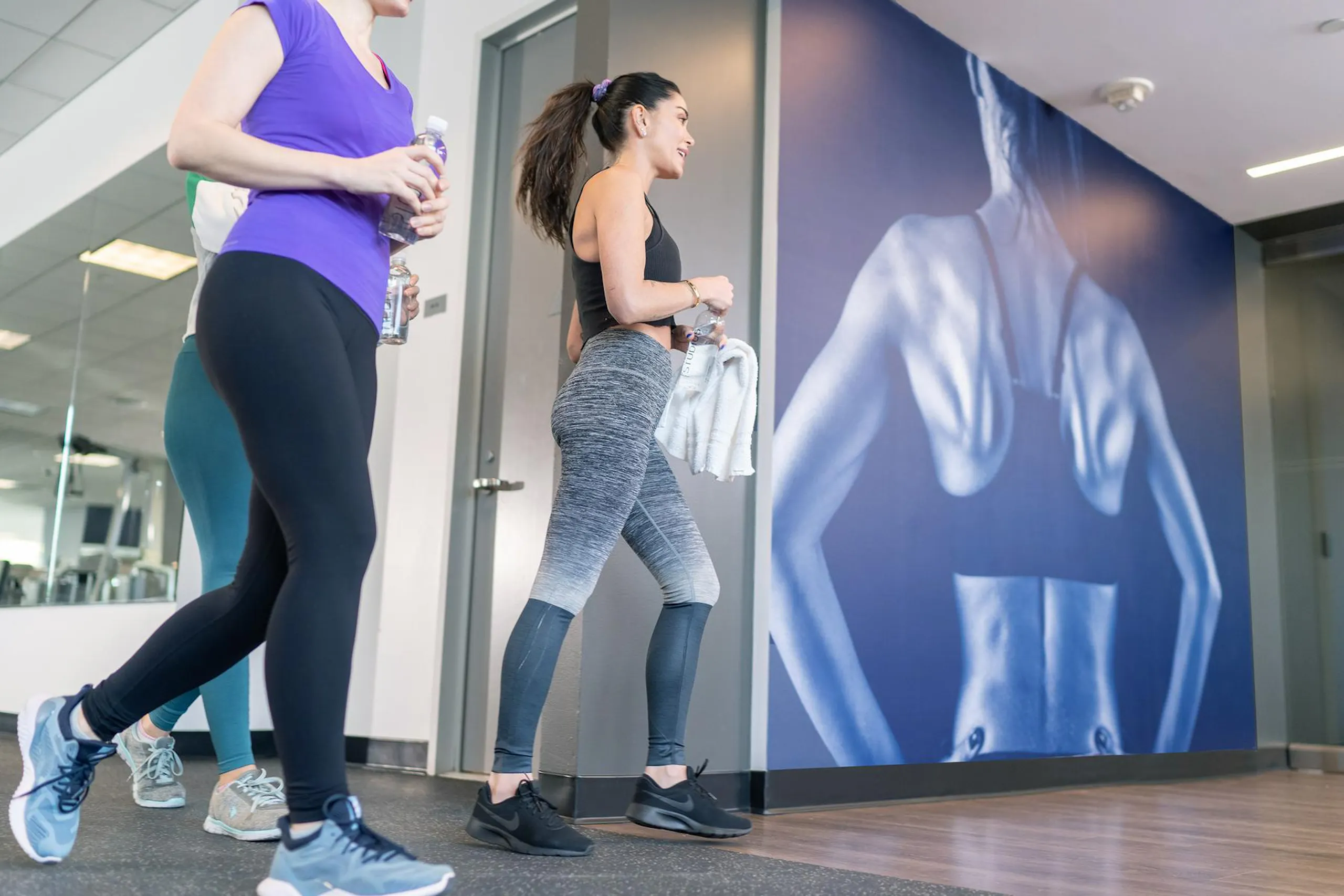 women in gym with big poster of lats on the wall