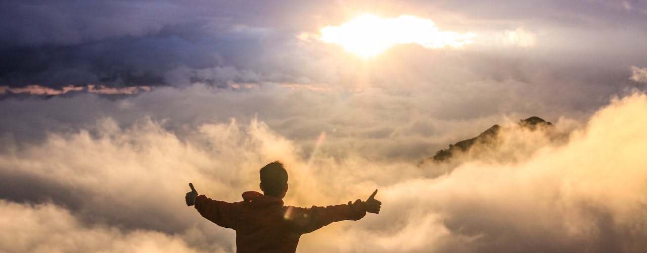 Man doing thumbs up standing on a mountain amongst the clouds