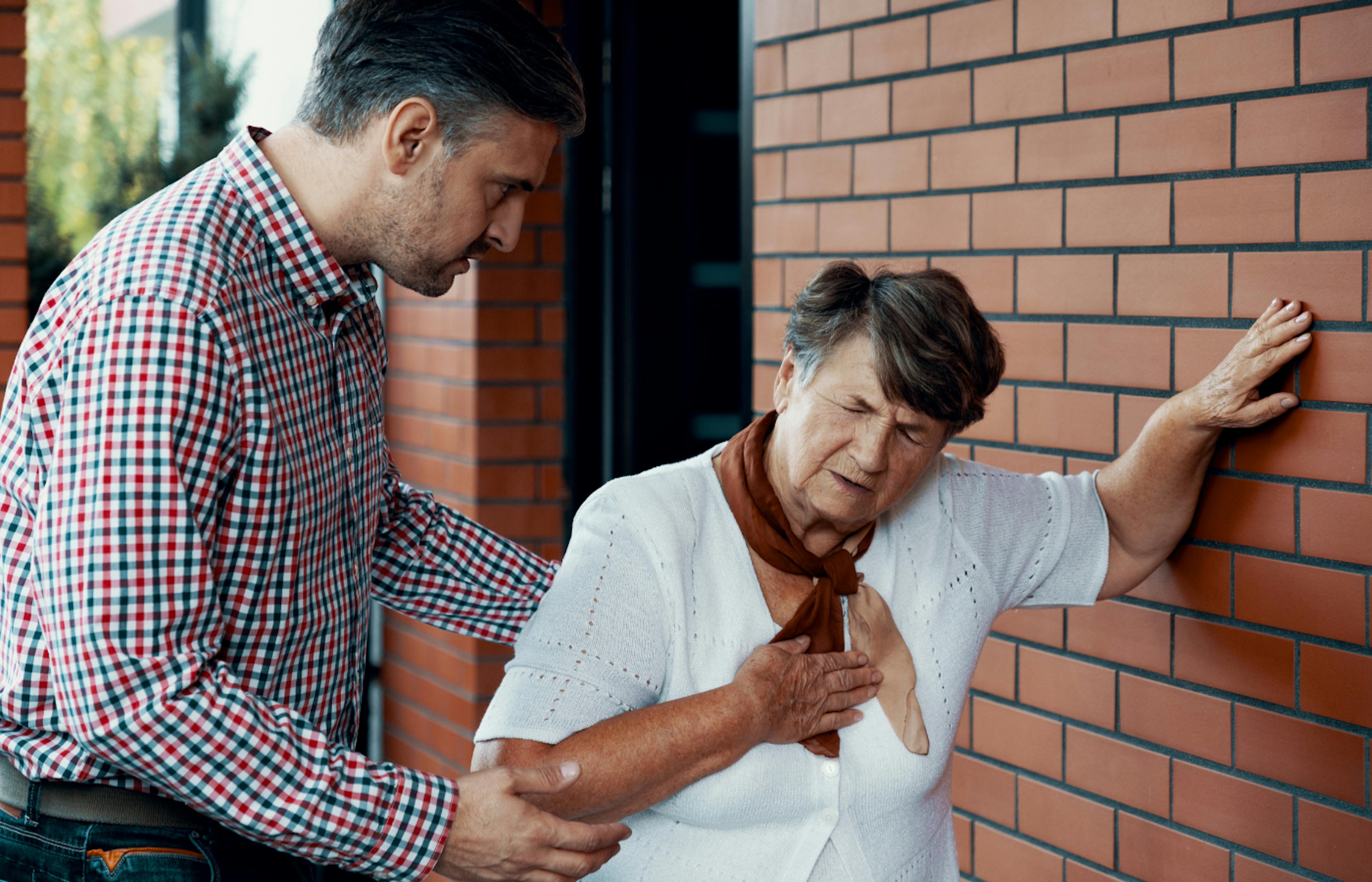 An elderly woman consoled by a middle-aged man as she experiences shortness of breath