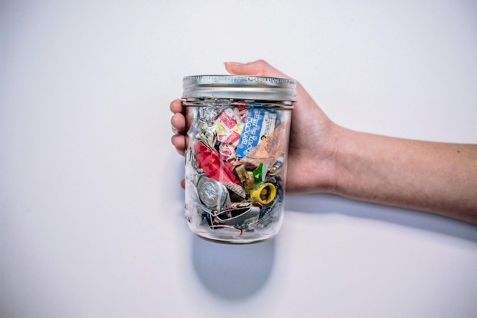 A person holding waste on a glass jar