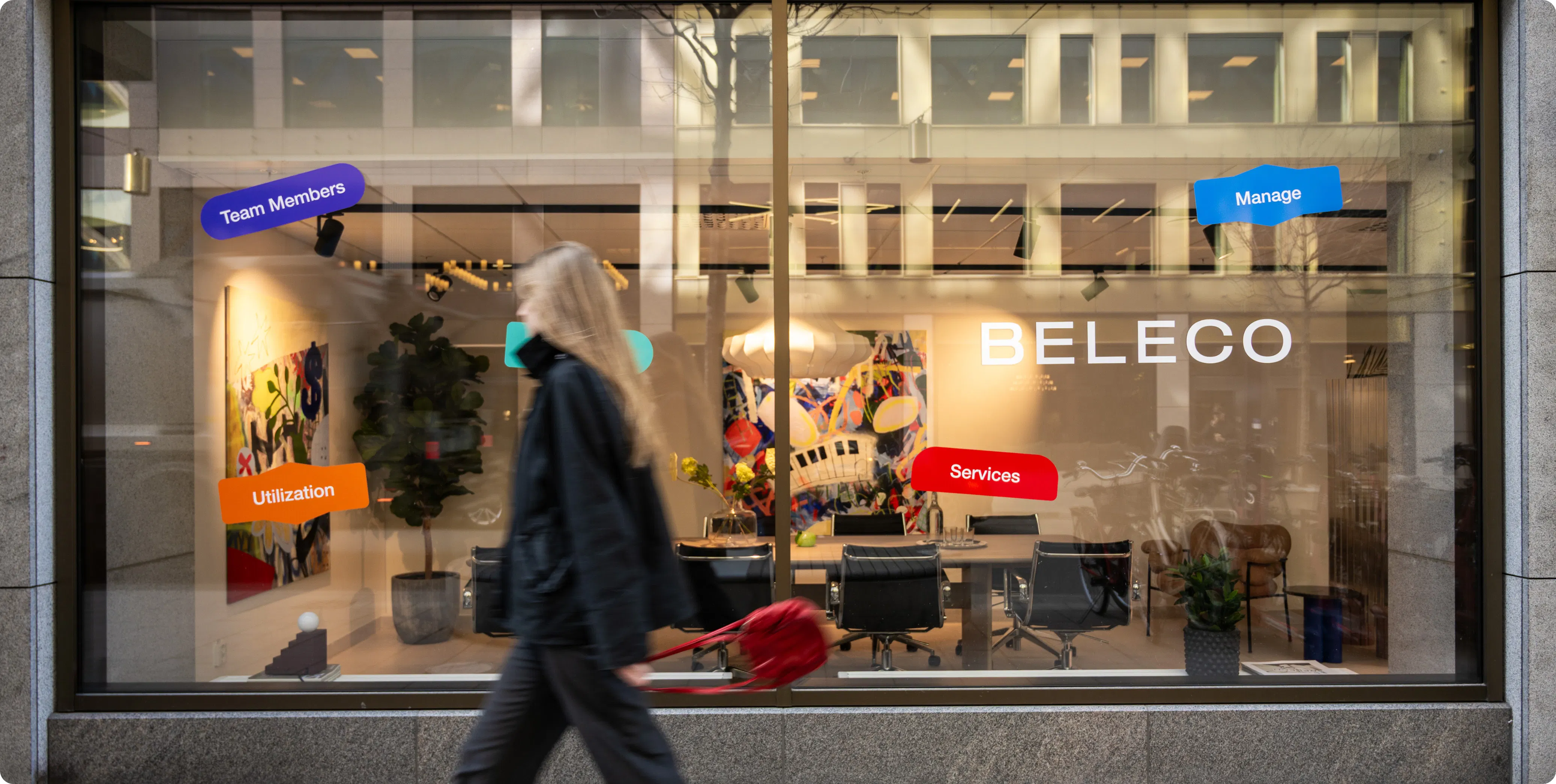 Fasadvy av Belecos showroom på Malmskillnadsgatan med stora glasfönster. Inne syns mötesbord, konstverk på väggarna och designmöbler. En person går förbi på trottoaren.