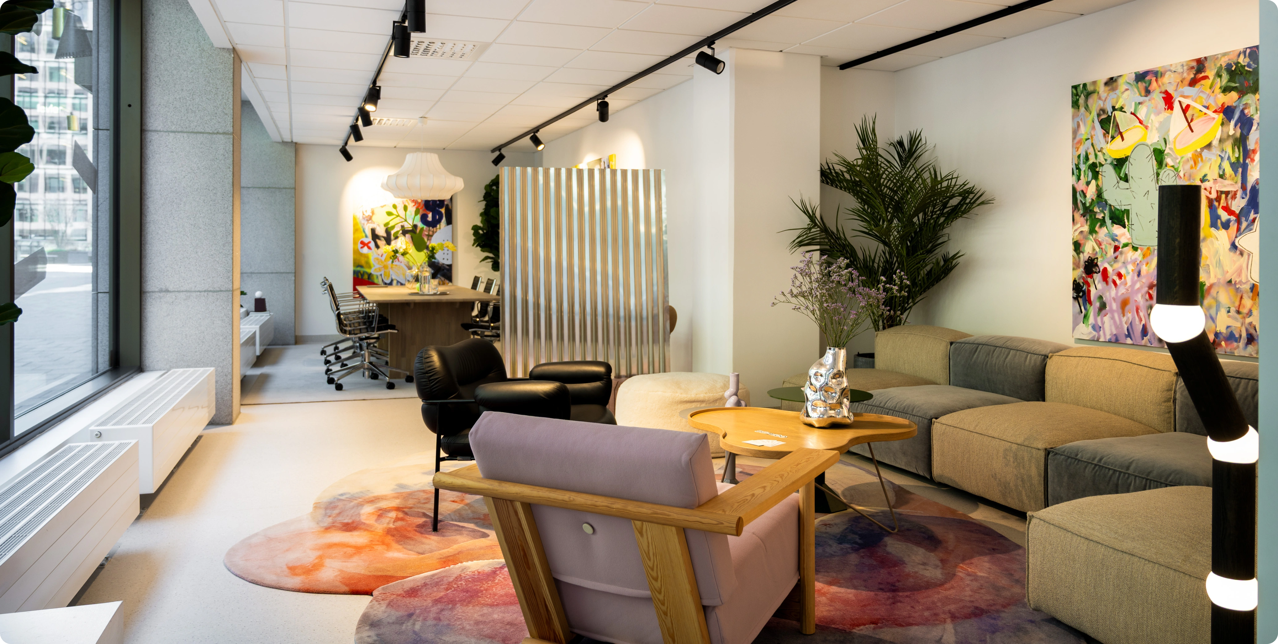 Lounge area with sofa, chairs, rugs, and colorful art on the wall.