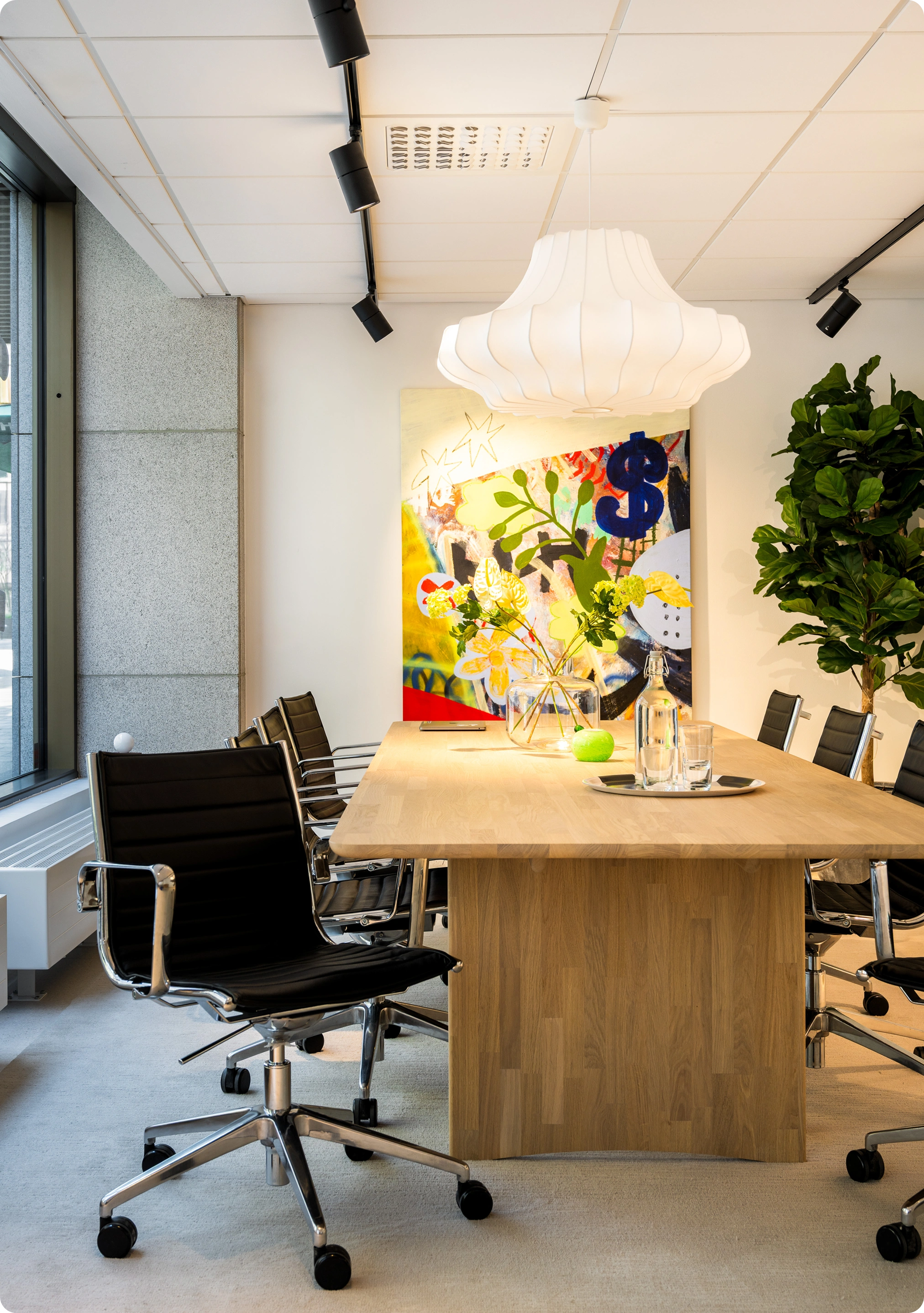 Meeting room with a wooden table, black chairs, and colorful art on the wall.
