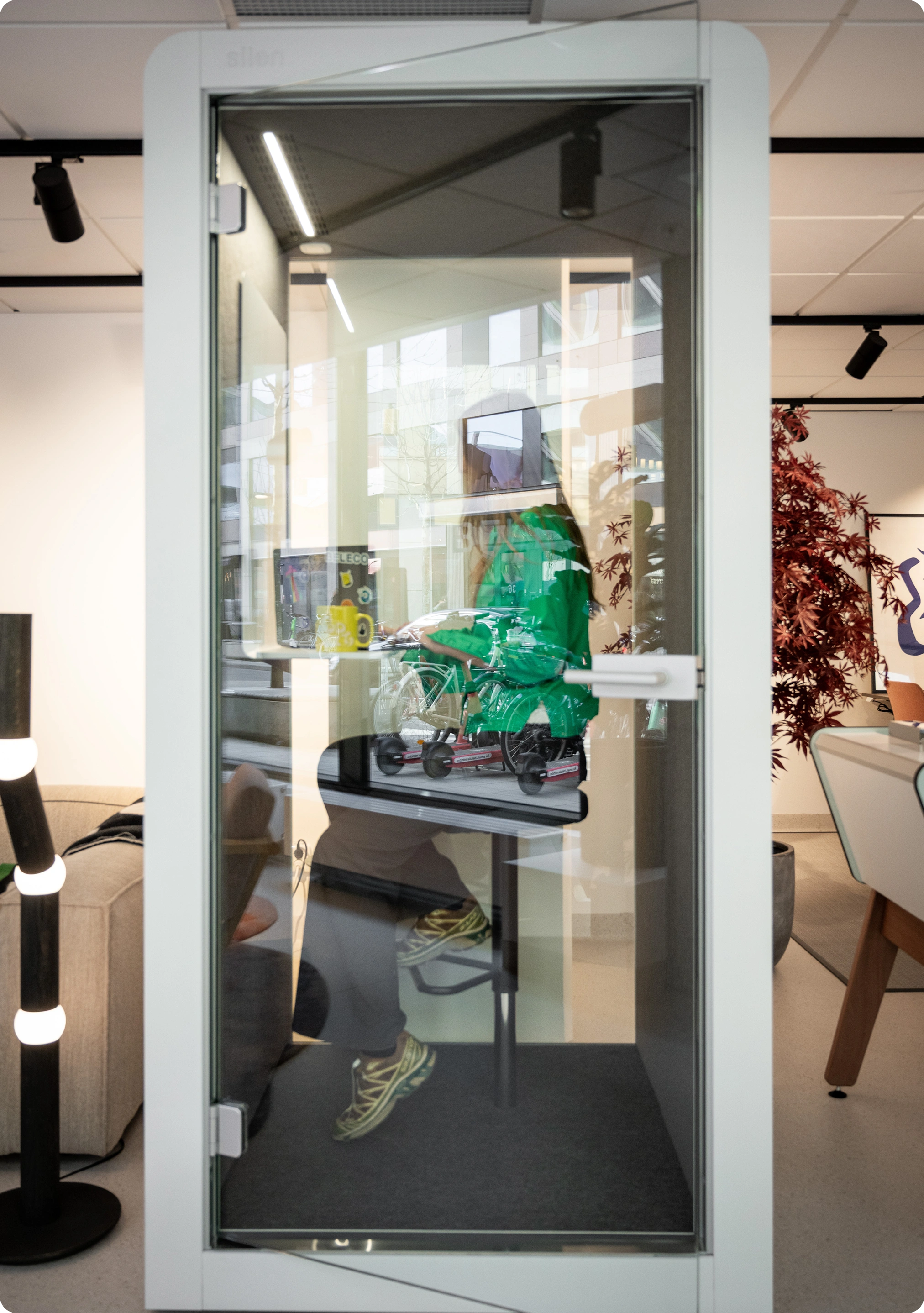 Phone booth with glass door. A person is sitting inside working.
