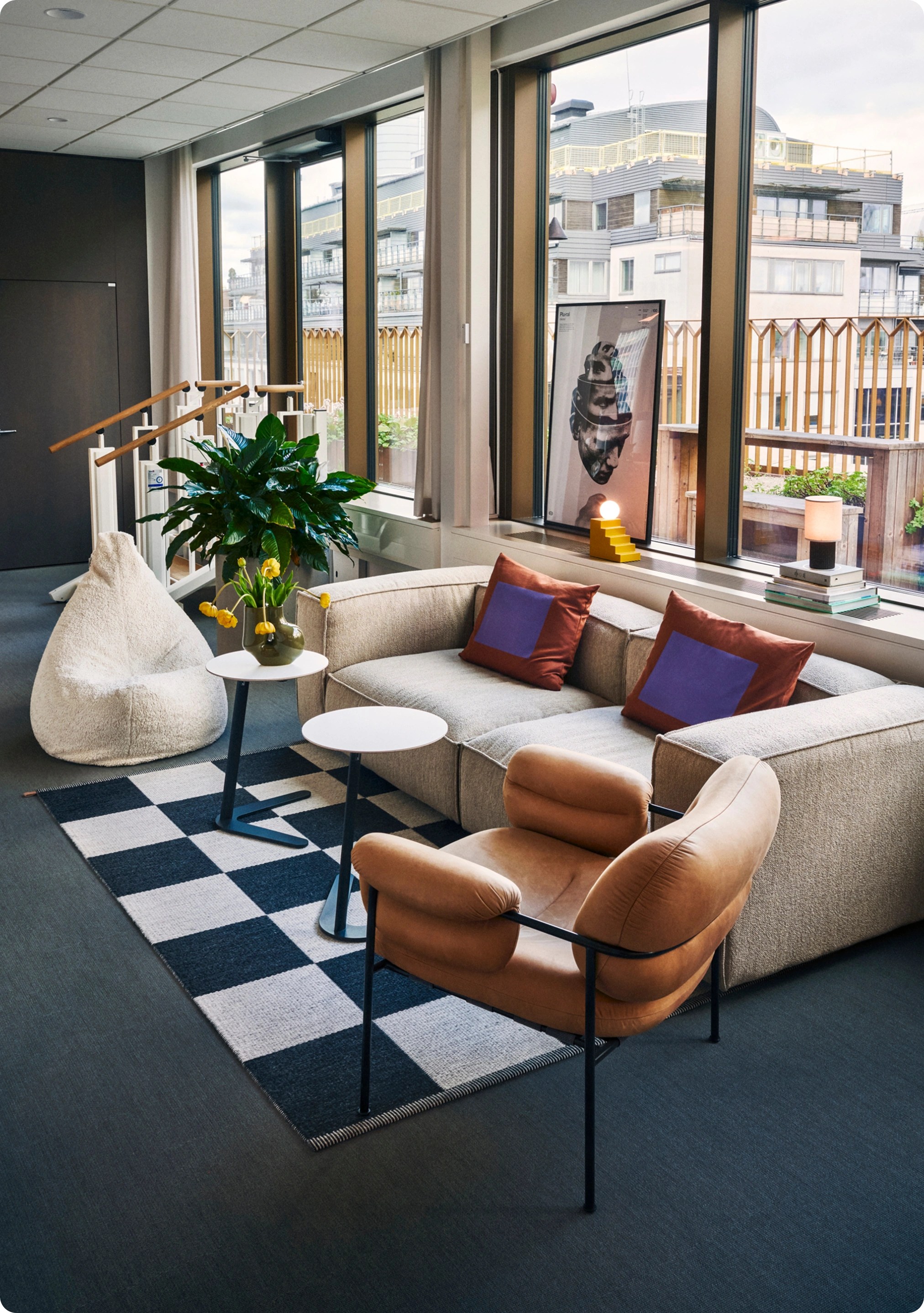 Lounge med beige soffa, brun fåtölj, rutigt golv och gröna växter vid stora fönster i Kings kontor.