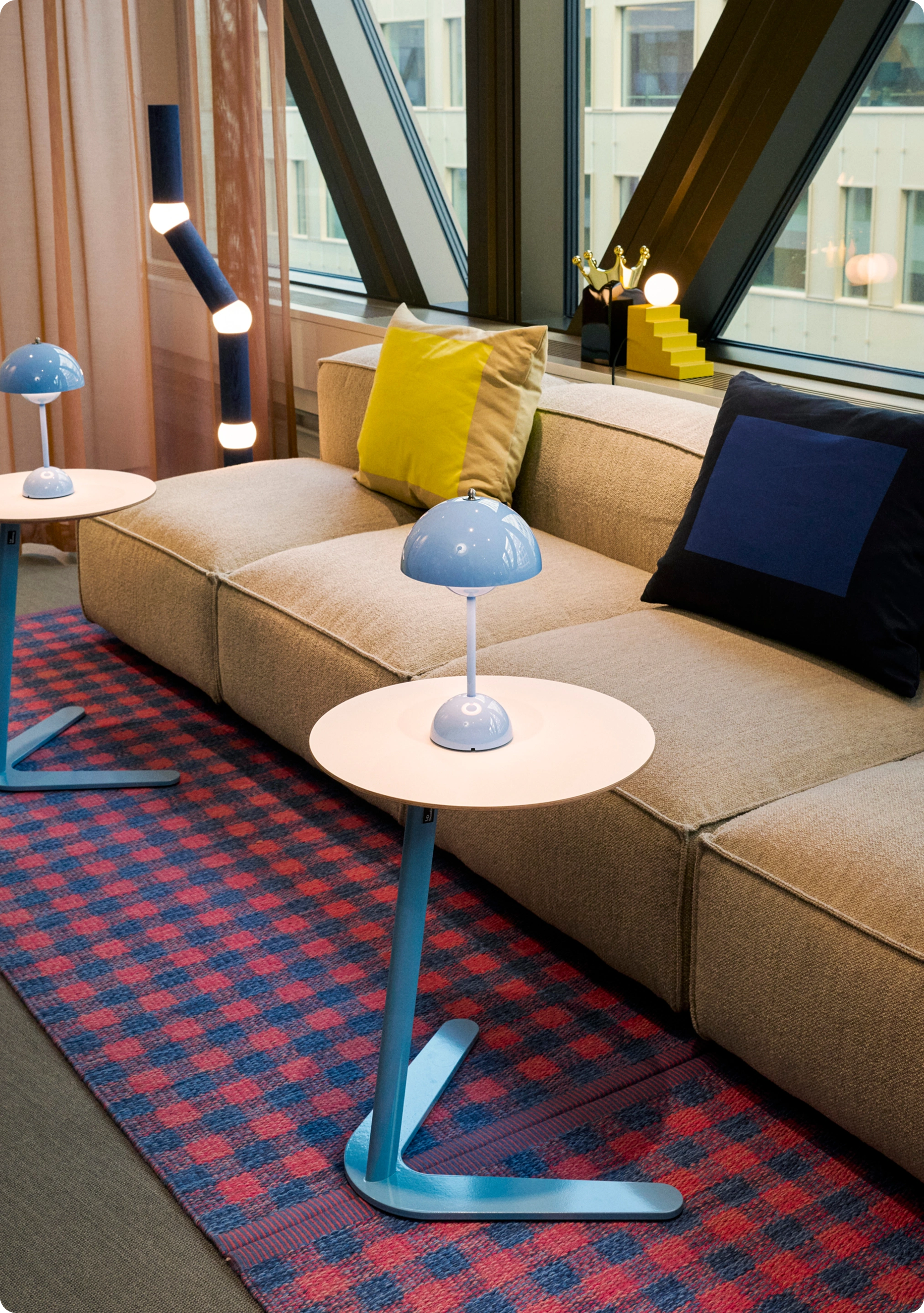 Beige soffa med blå kuddar, sittpuff och rutig matta i loungeområde på Kings kontor.
