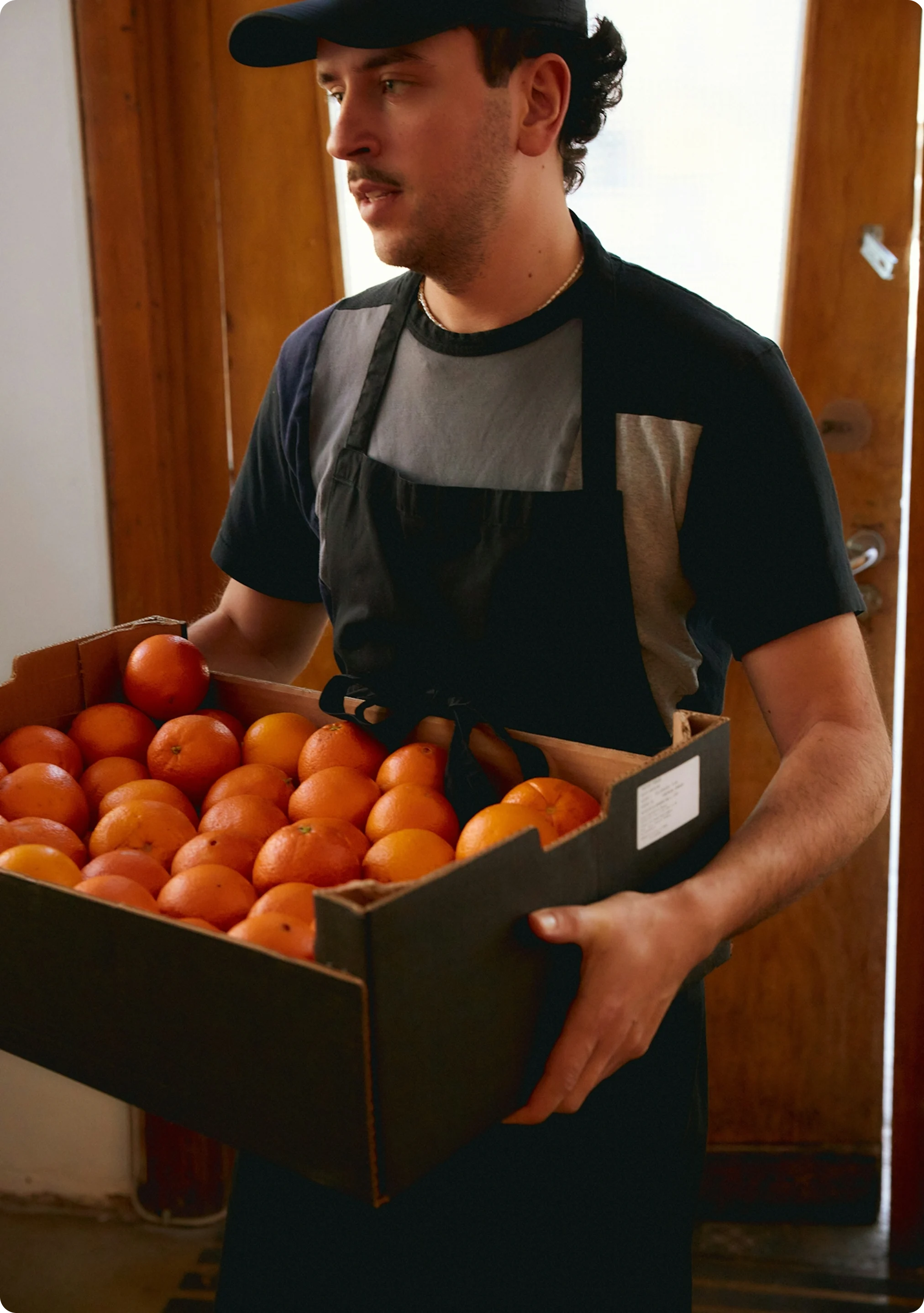 A worker carrying a crate full of oranges – symbol of FM services like office fruit delivery.